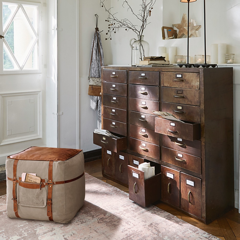 Commode vintage en métal avec plusieurs tiroirs et pouf beige à sangles marron dans un intérieur lumineux