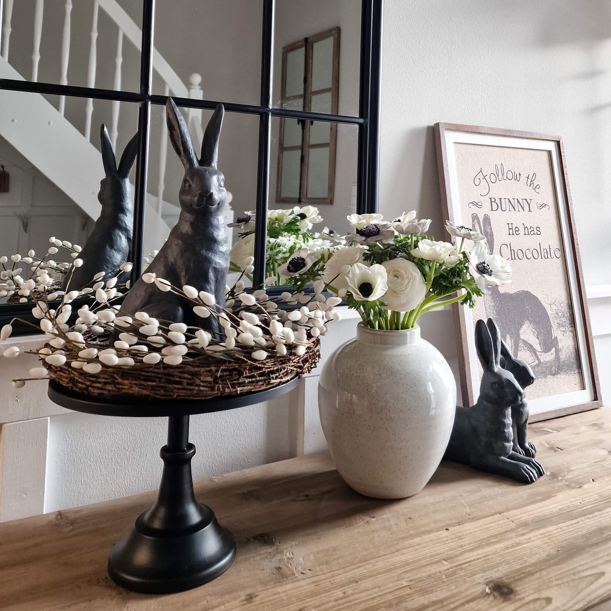 Lapin décoratif noir avec couronne en osier et fleurs blanches dans un vase en céramique sur une table en bois