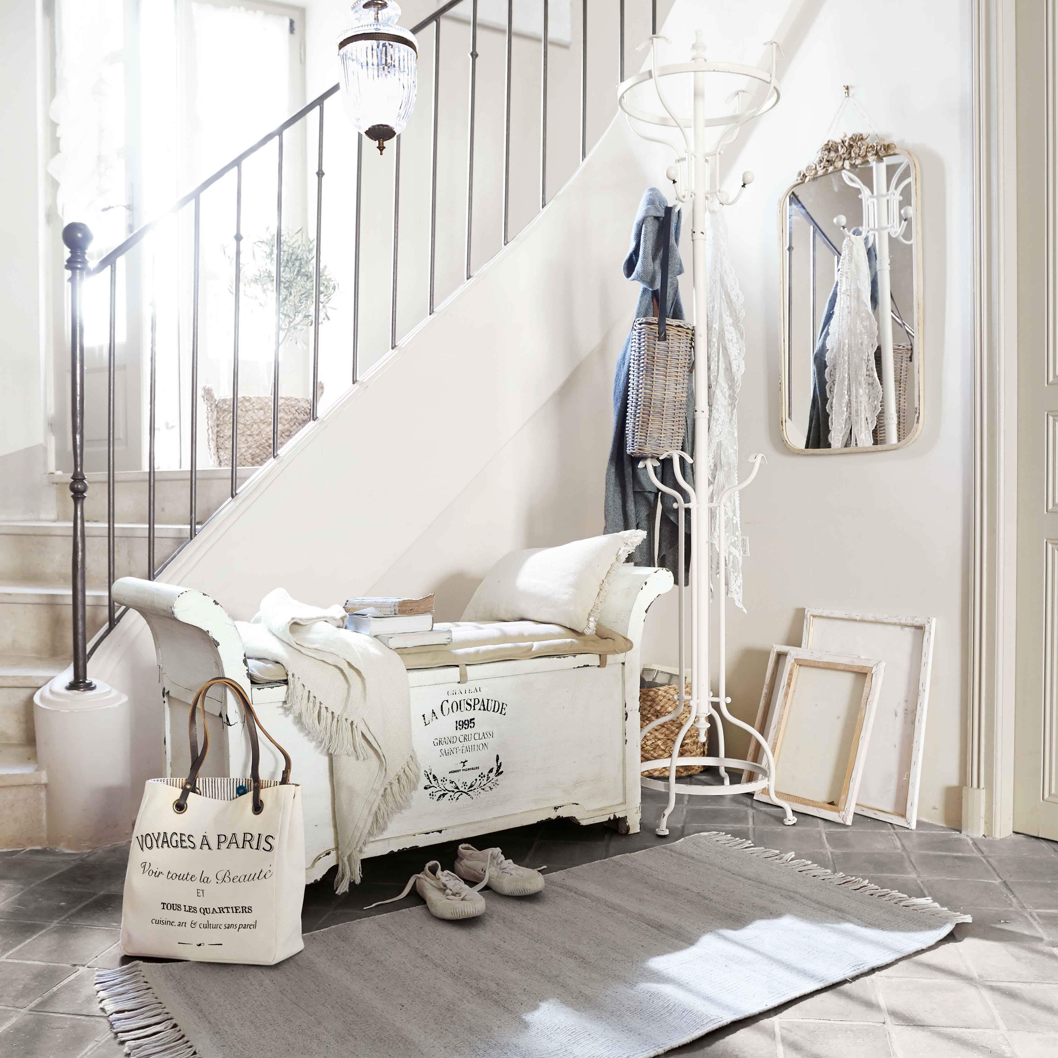 Banc en bois blanc avec coussin et plaid dans un hall lumineux avec porte-manteau et miroir