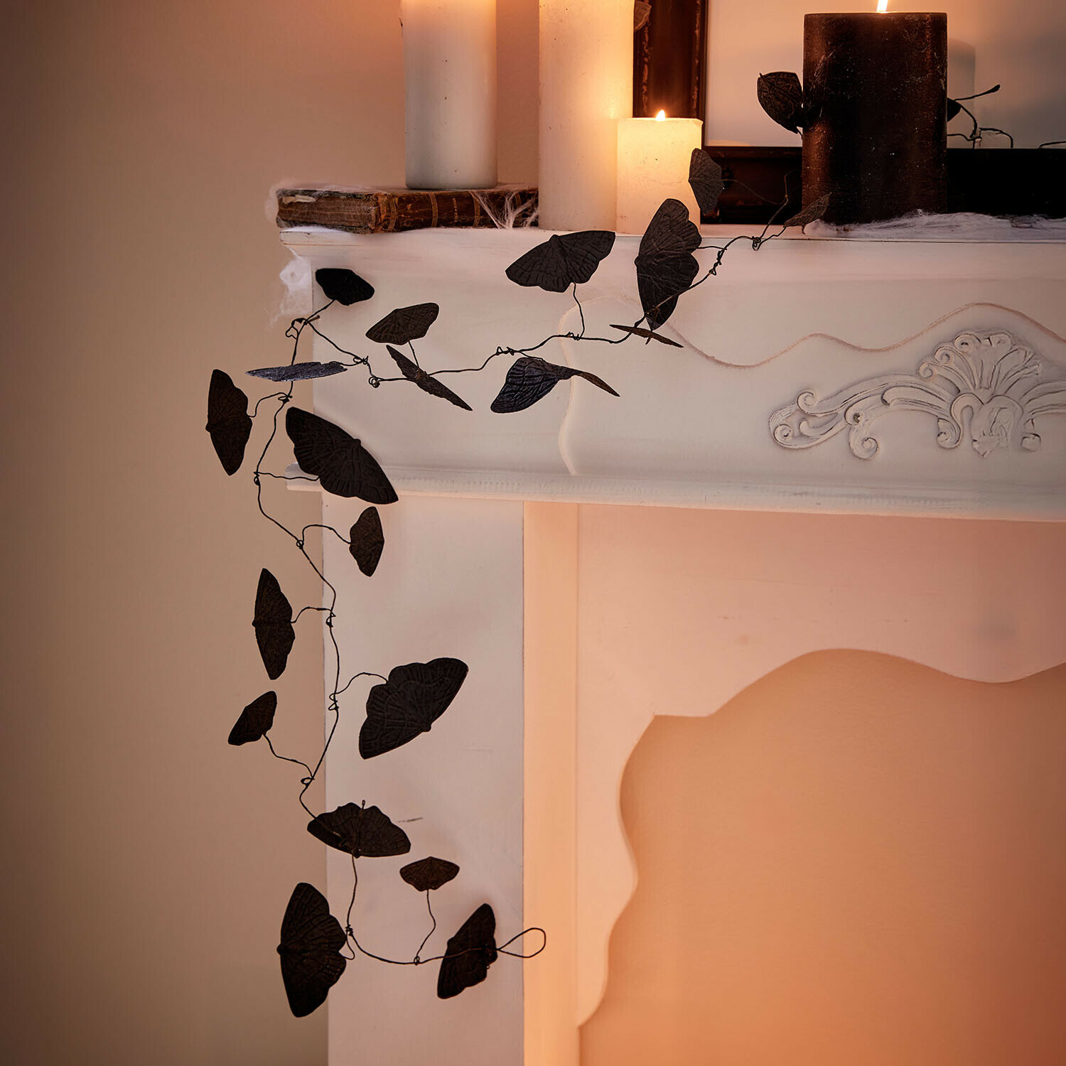 Guirlande Orlenaith Guirlande noire décorative en forme de feuilles sur une cheminée blanche avec des bougies allumées