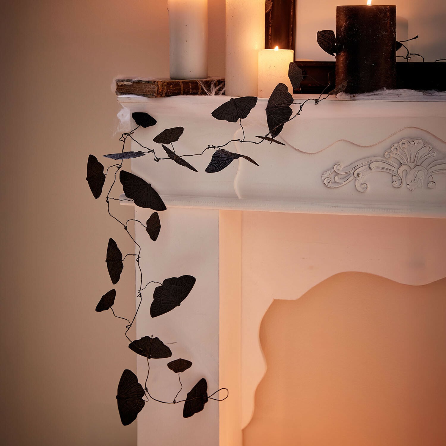 Guirlande Orlenaith Guirlande noire décorative en forme de feuilles sur une cheminée blanche avec des bougies allumées