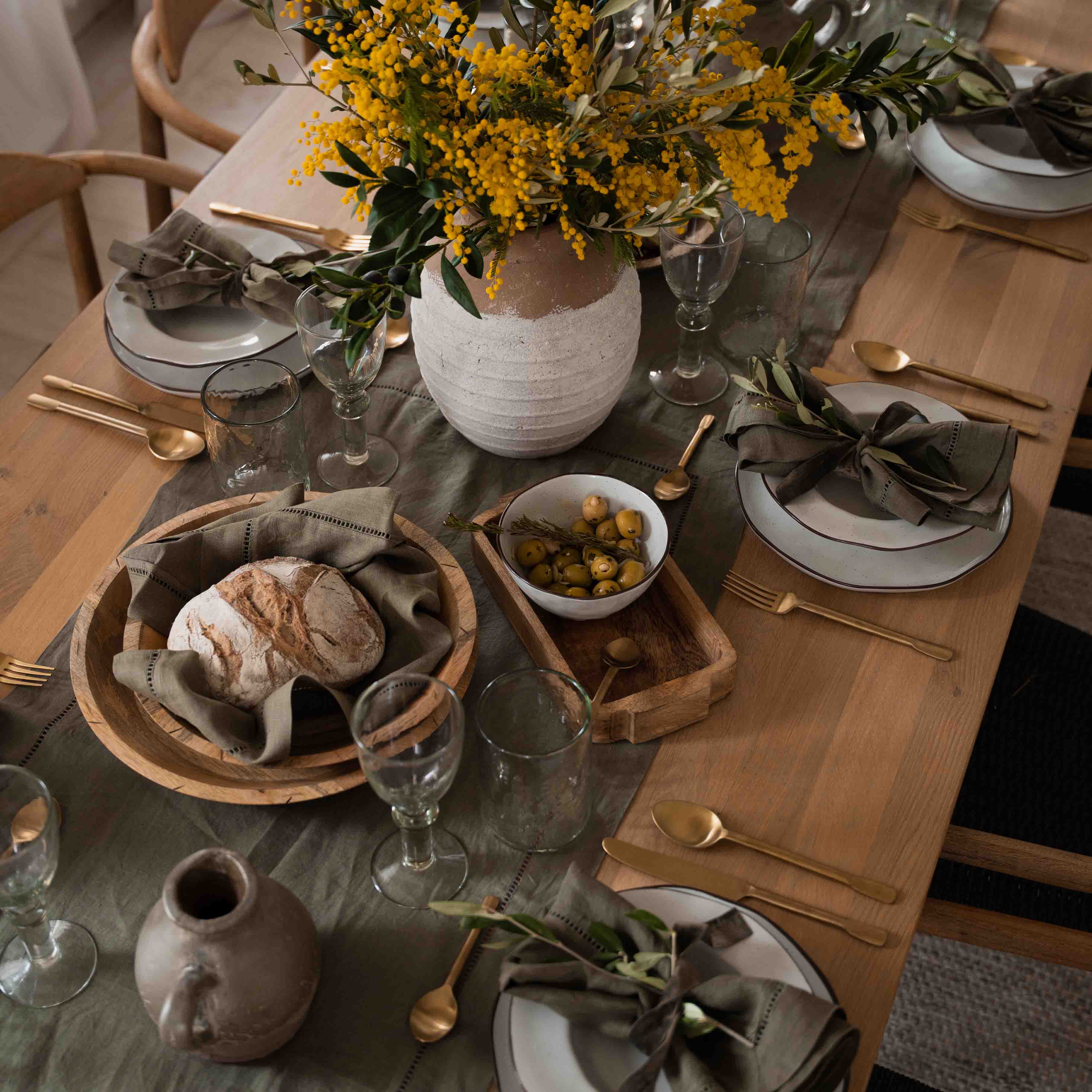 Table rustique en bois avec vaisselle blanche, serviettes vertes et bouquet de fleurs jaunes en pot en argile