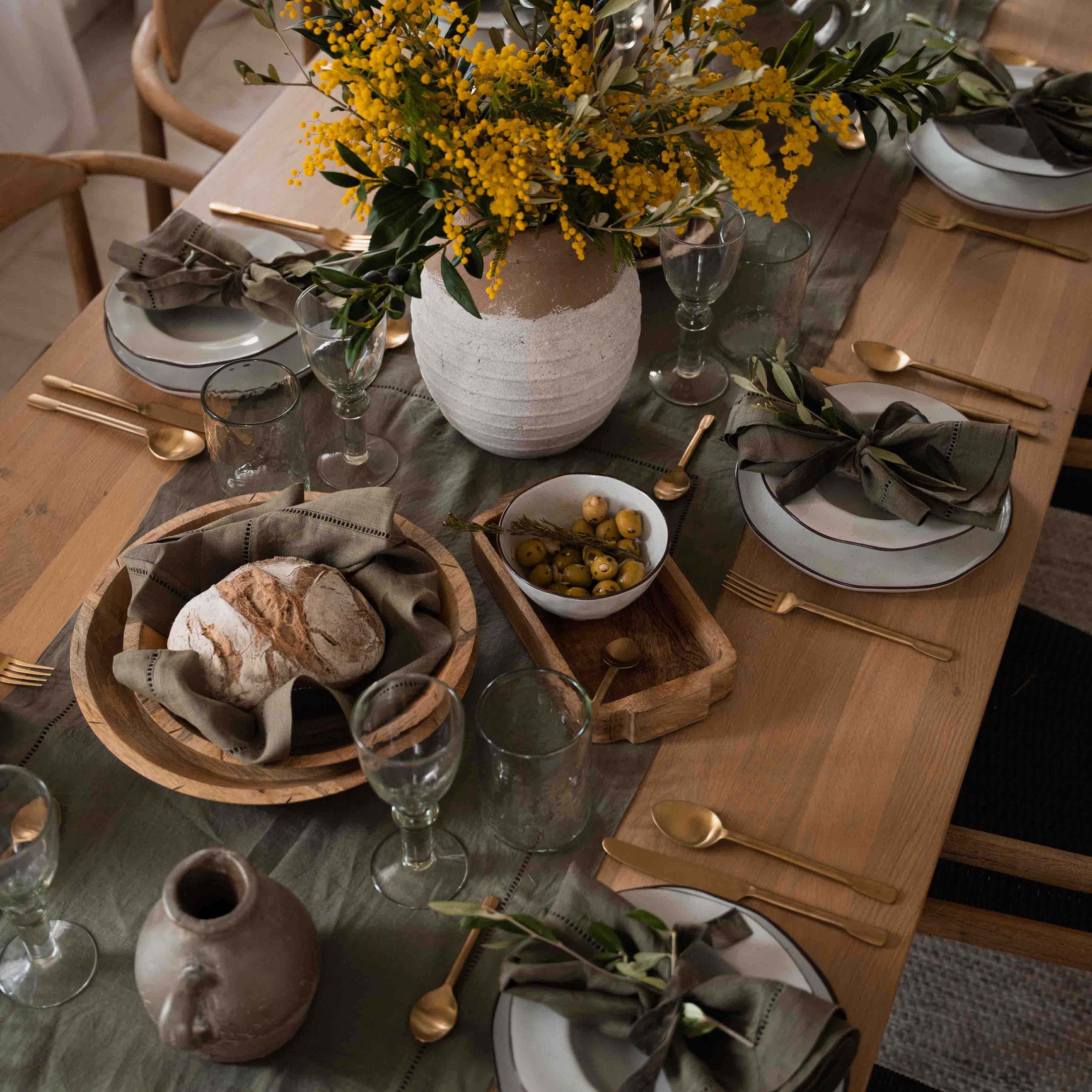 Table rustique en bois avec vaisselle blanche, serviettes vertes et bouquet de fleurs jaunes en pot en argile