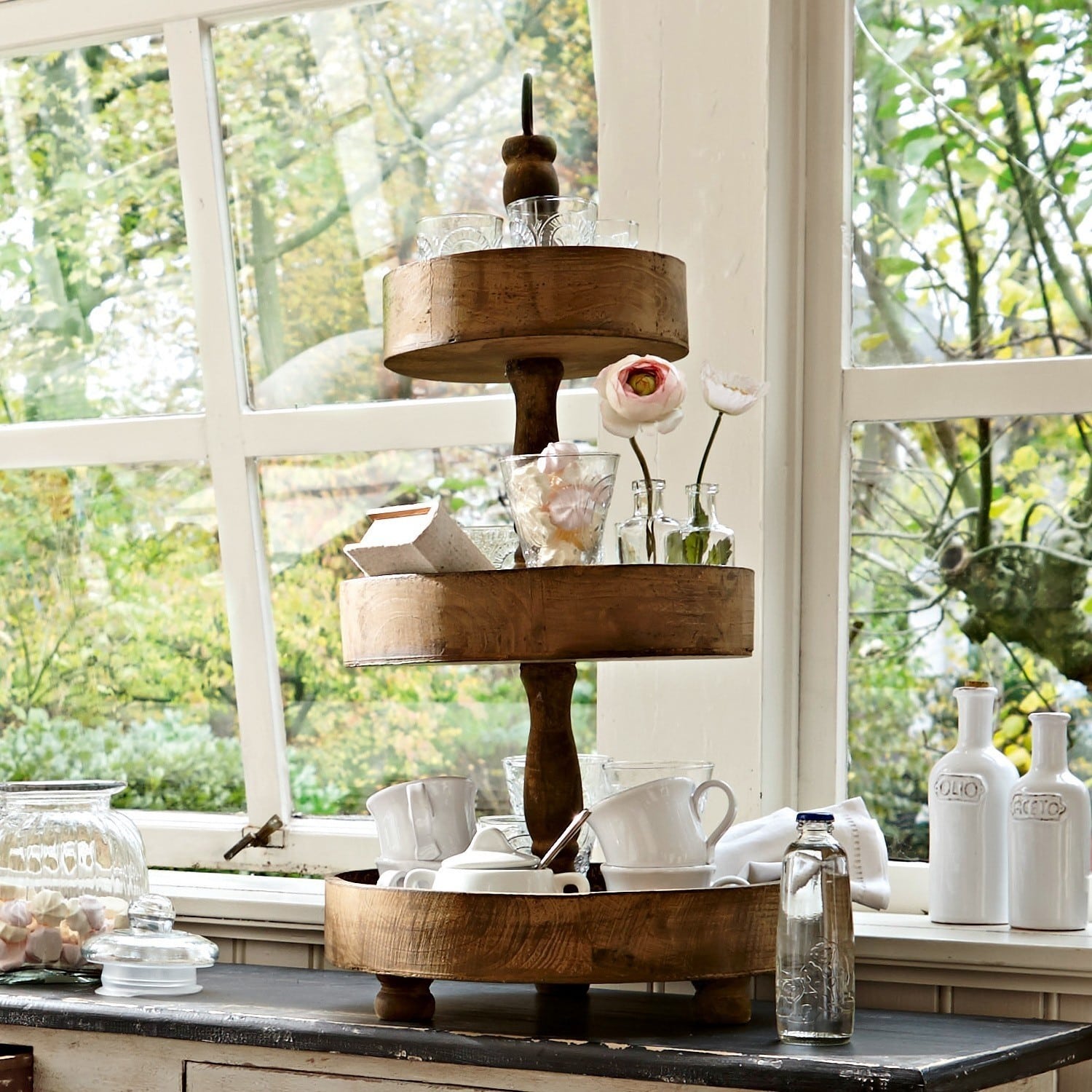 Présentoir à étages Beauvais Présentoir à trois niveaux en bois naturel avec tasses et décorations devant une fenêtre avec vue sur jardin