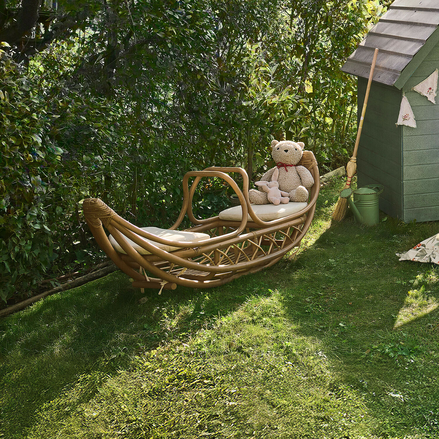 Chaise longue en rotin naturel avec coussins clairs posée sur l'herbe dans un jardin