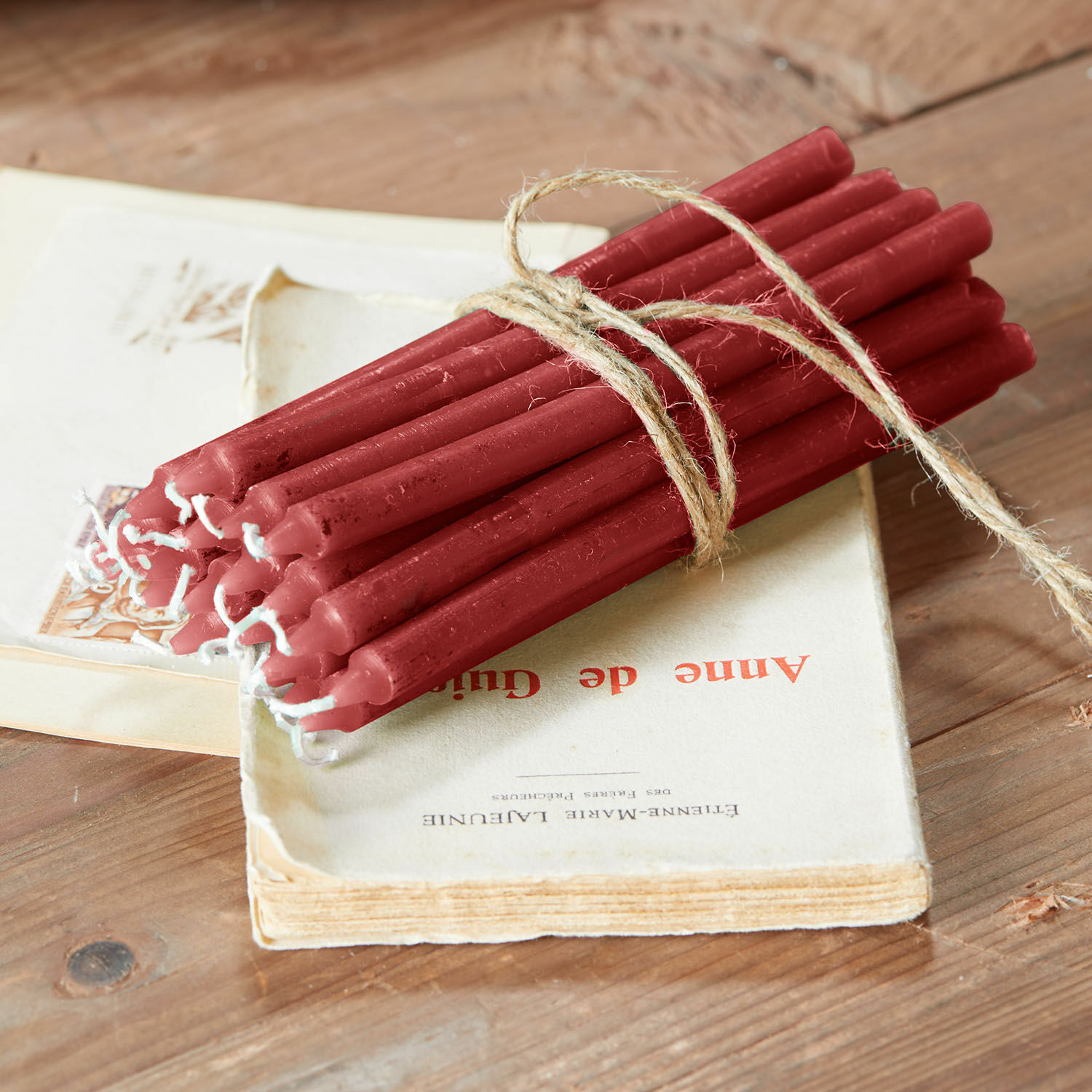 Lot de 20 bougies Lysarion Lot de bougies rouges en cire liées par une corde sur une table en bois avec un livre ancien