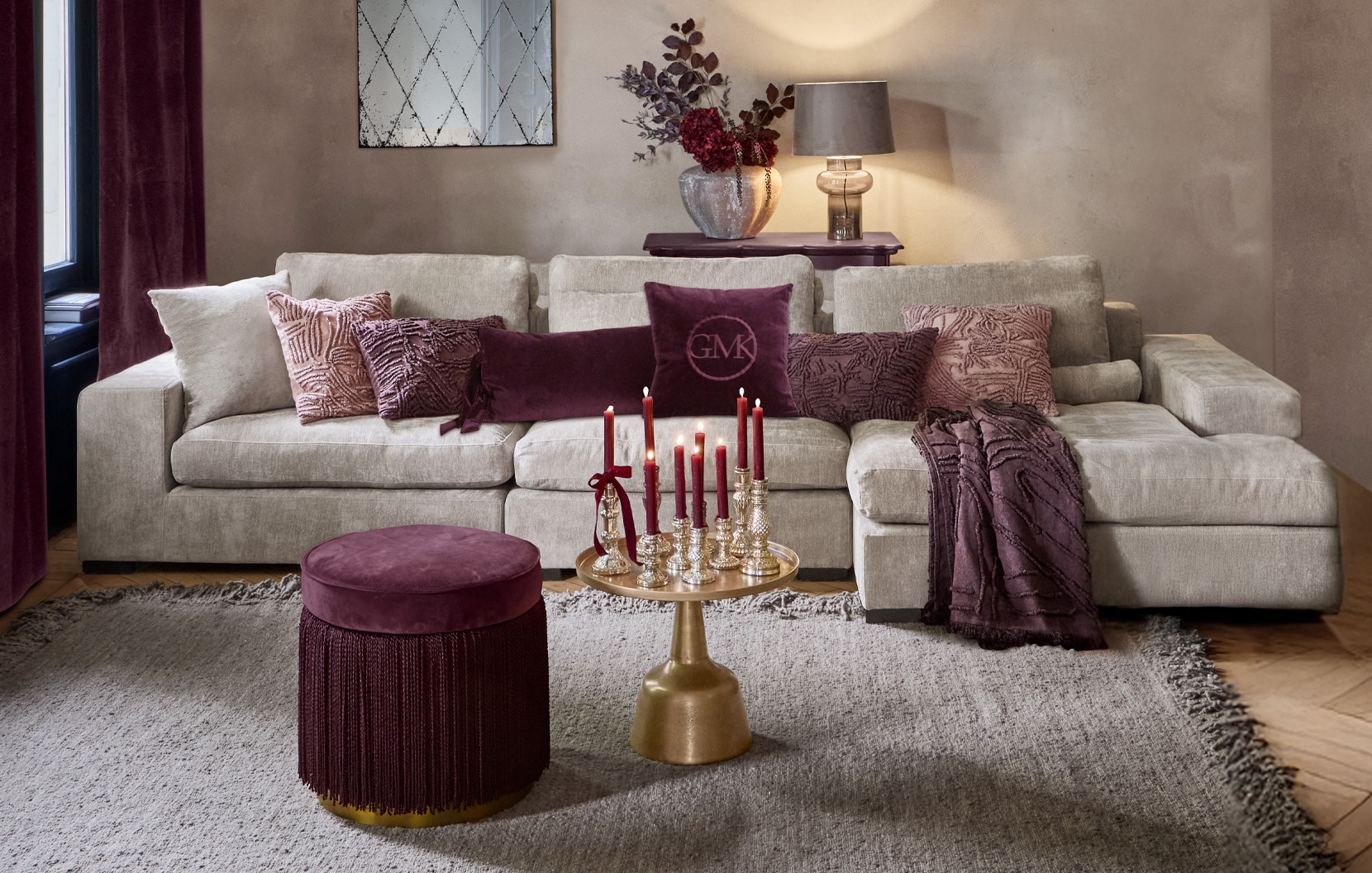 Canapé beige avec coussins violets et pouf bordeaux dans un salon élégant avec bougies décoratives