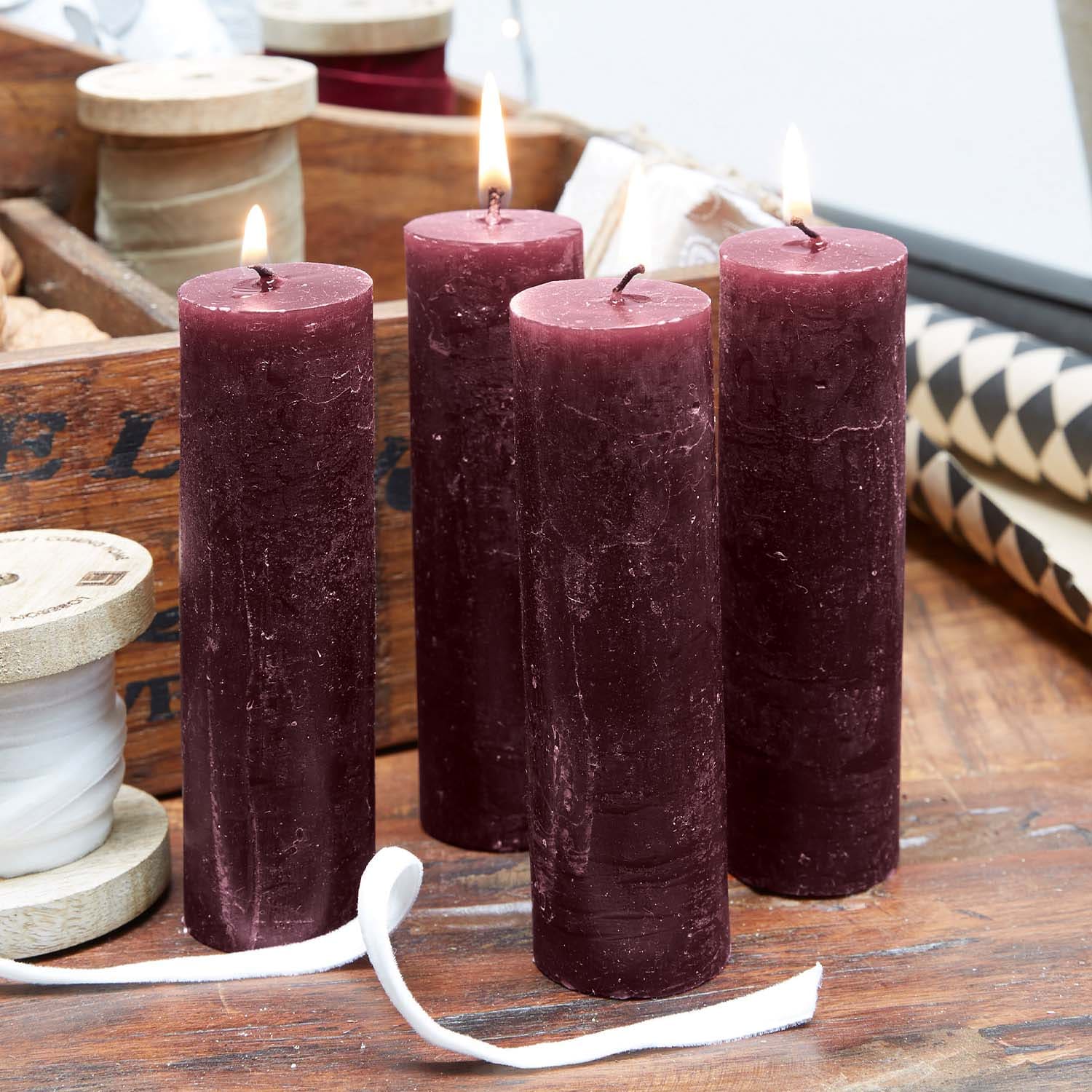 Quatre bougies cylindriques bordeaux en cire sur une table en bois, décoration chaleureuse