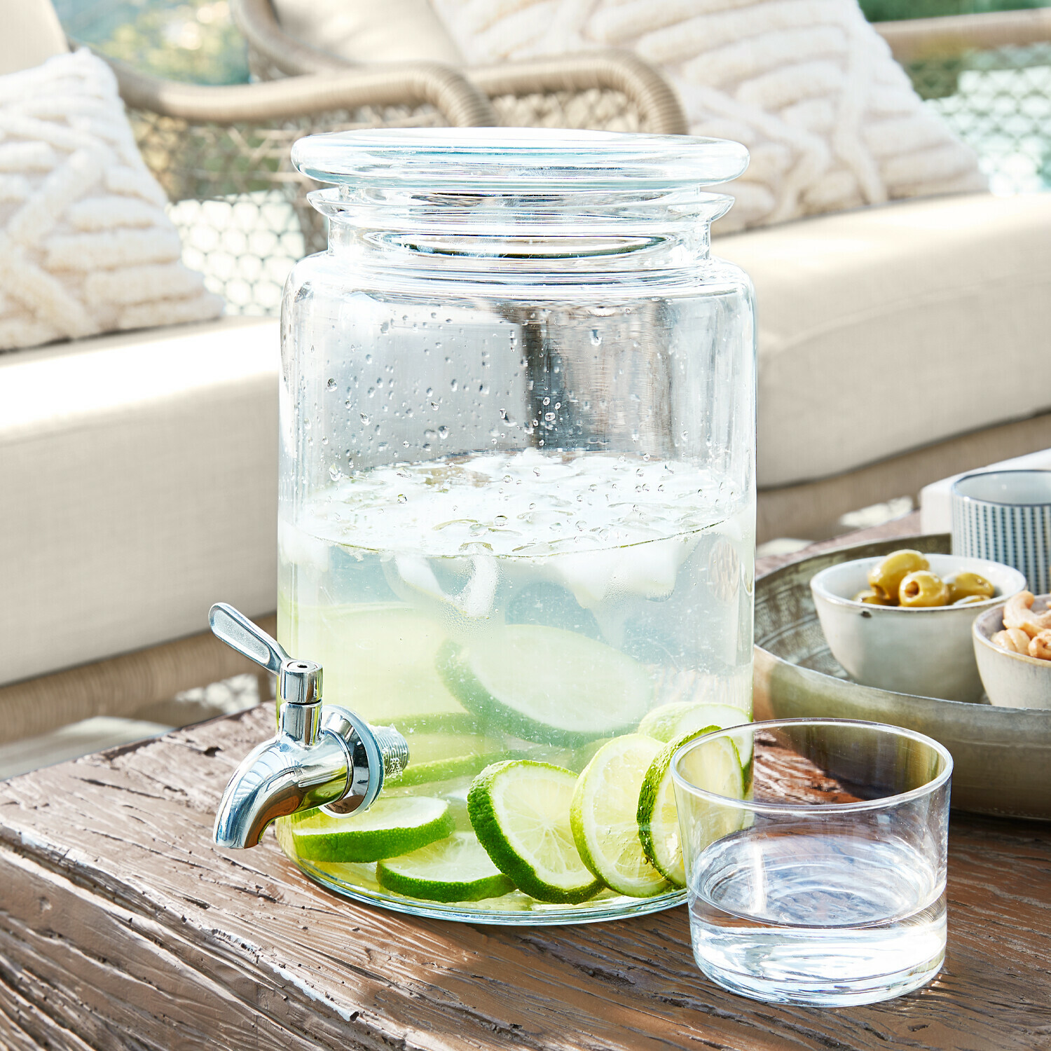 Distributeur de boisson en verre avec robinet, rempli d'eau citronnée, posé sur une table en bois