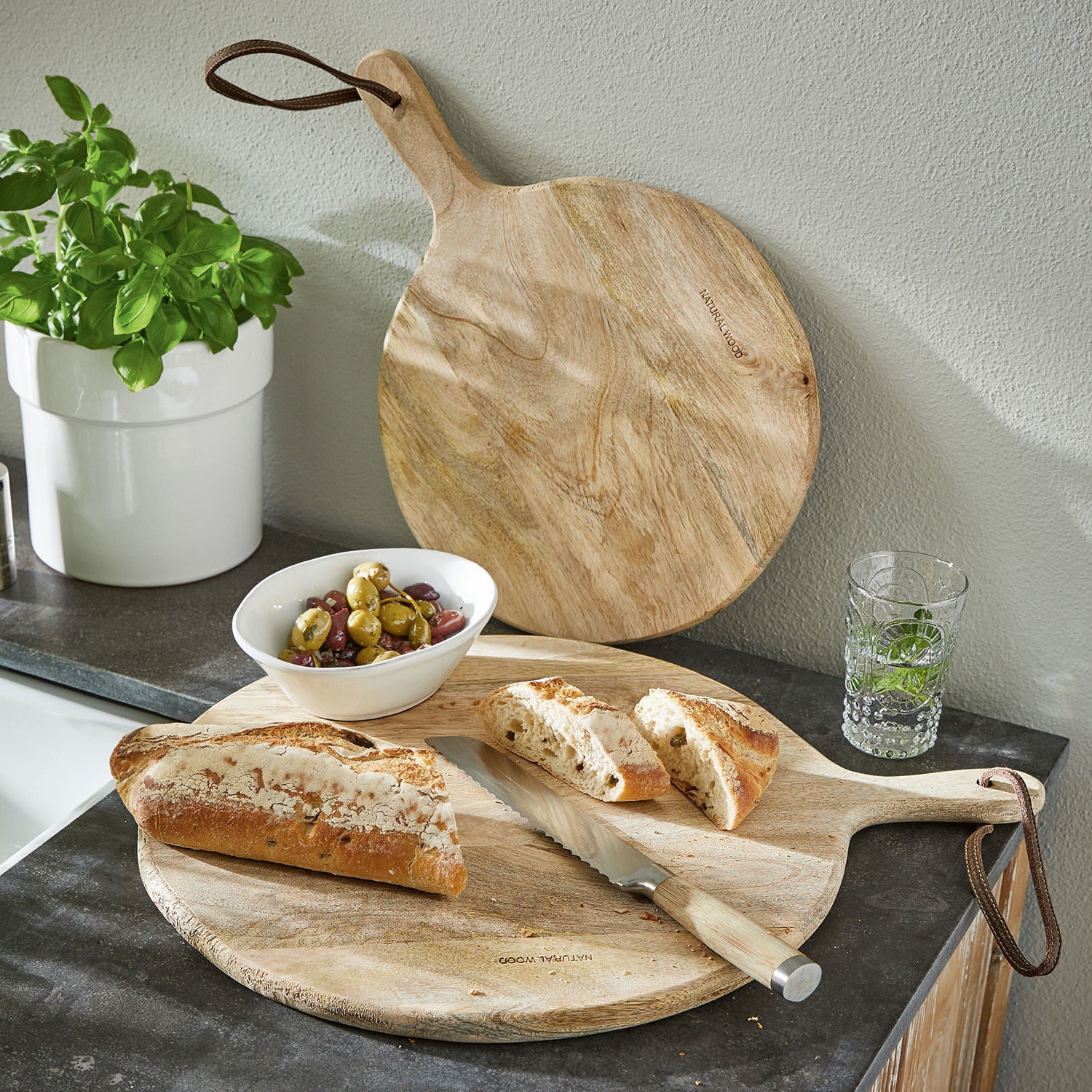 Lot de 2 planches à découper Nitra Planche à découper en bois naturel avec poignée, couteau à pain, pain tranché et olives sur un comptoir