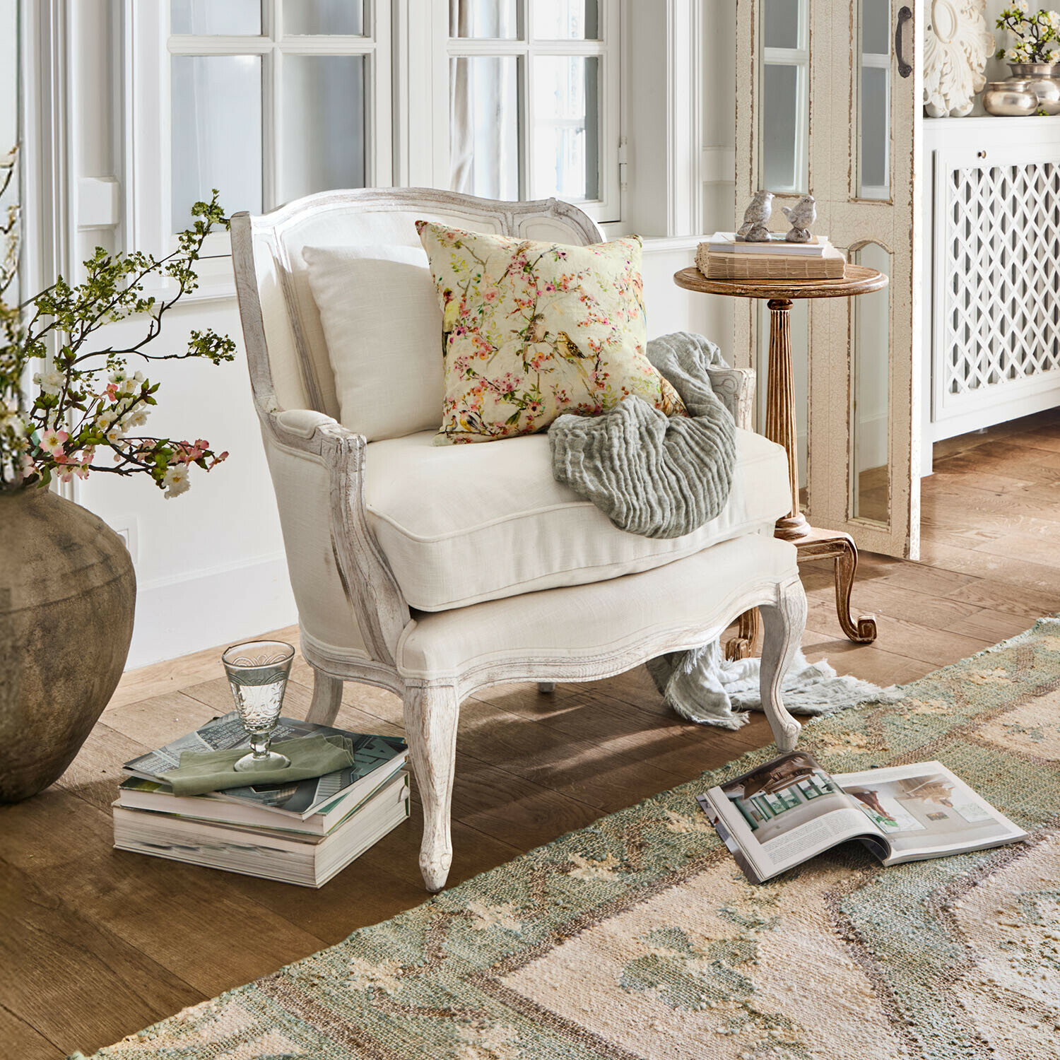 Fauteuil Kingswinford Fauteuil en bois blanc avec coussin fleuri et plaid gris dans un salon lumineux et chaleureux