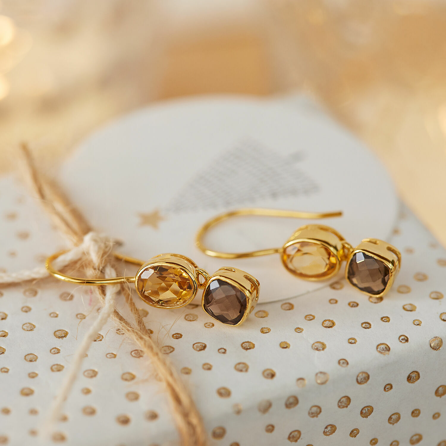 Boucles d'oreilles Ovique Boucles d'oreilles dorées avec pierres facettées marron posées sur un papier cadeau décoré