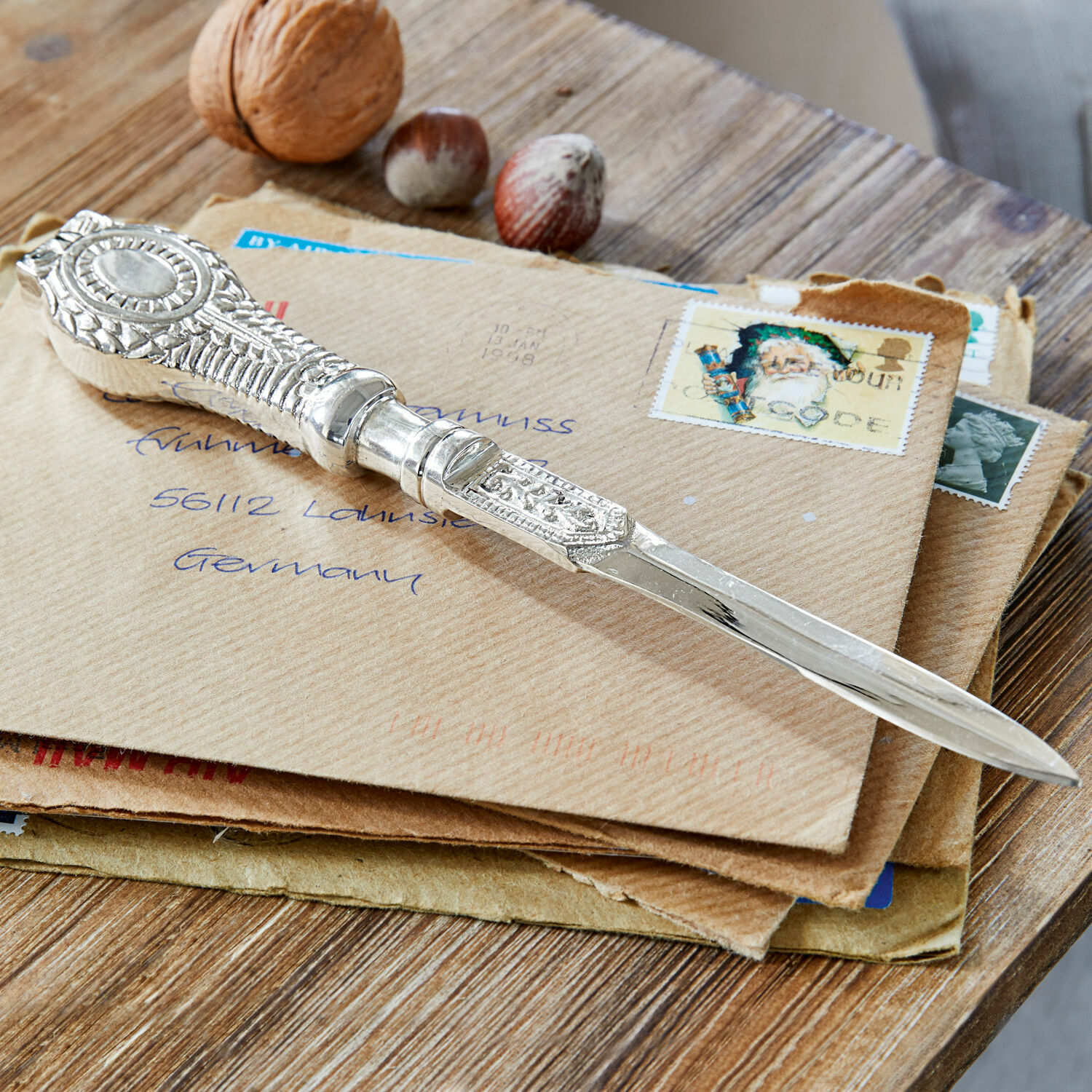Ouvre-lettres Parsifal Couteau à lettres argenté orné posé sur des enveloppes avec des noix sur une table en bois