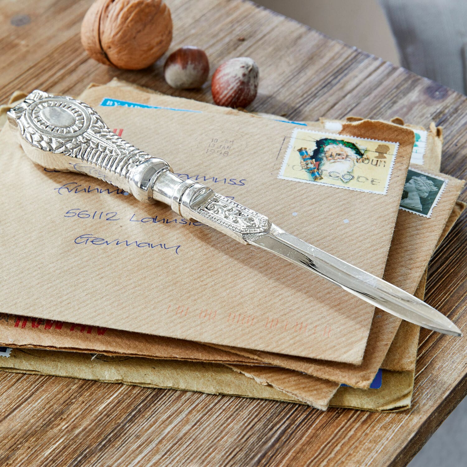 Ouvre-lettres Parsifal Couteau à lettres argenté orné posé sur des enveloppes avec des noix sur une table en bois