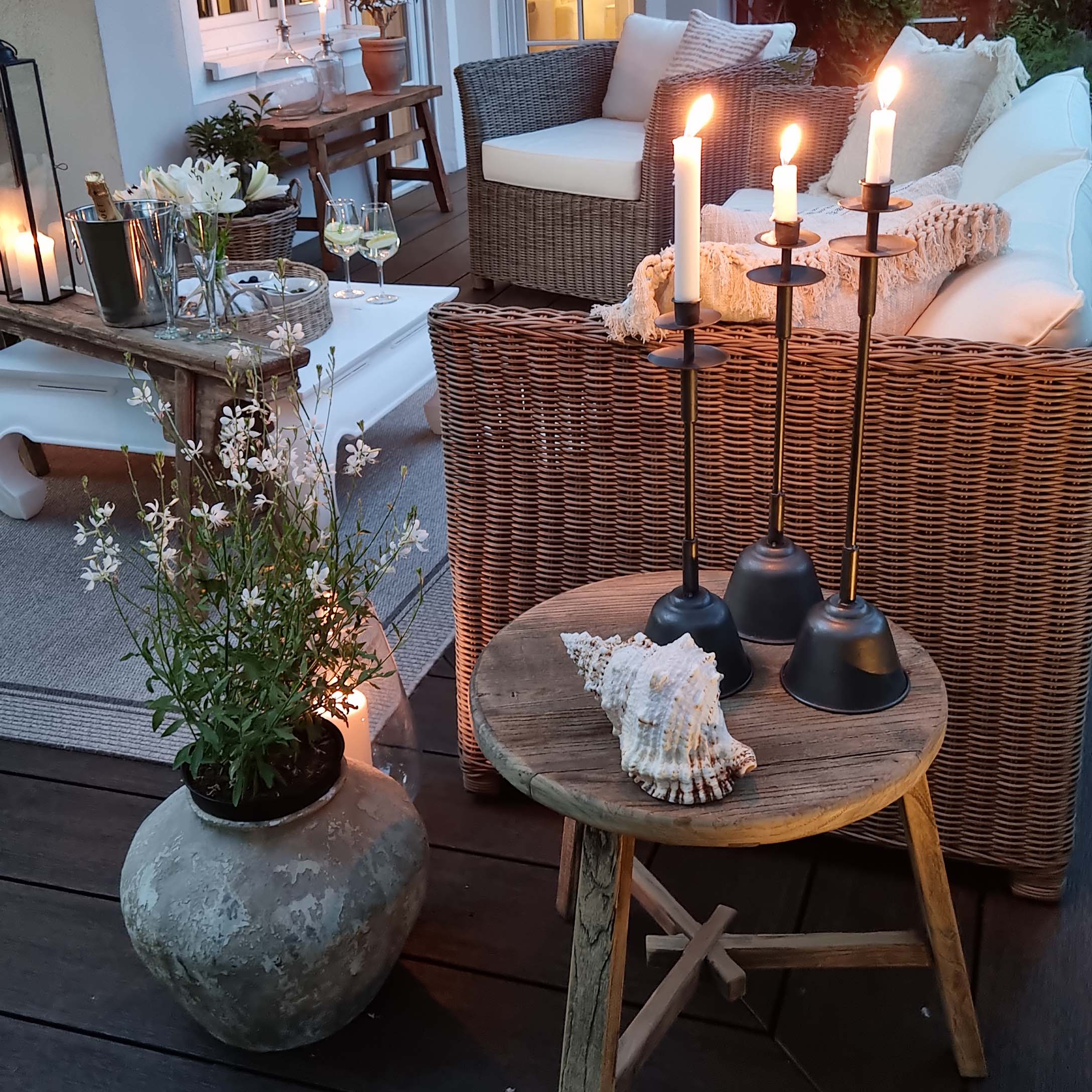 Terrasse accueillante avec canapé en osier, table en bois et bougeoirs en métal avec bougies blanches