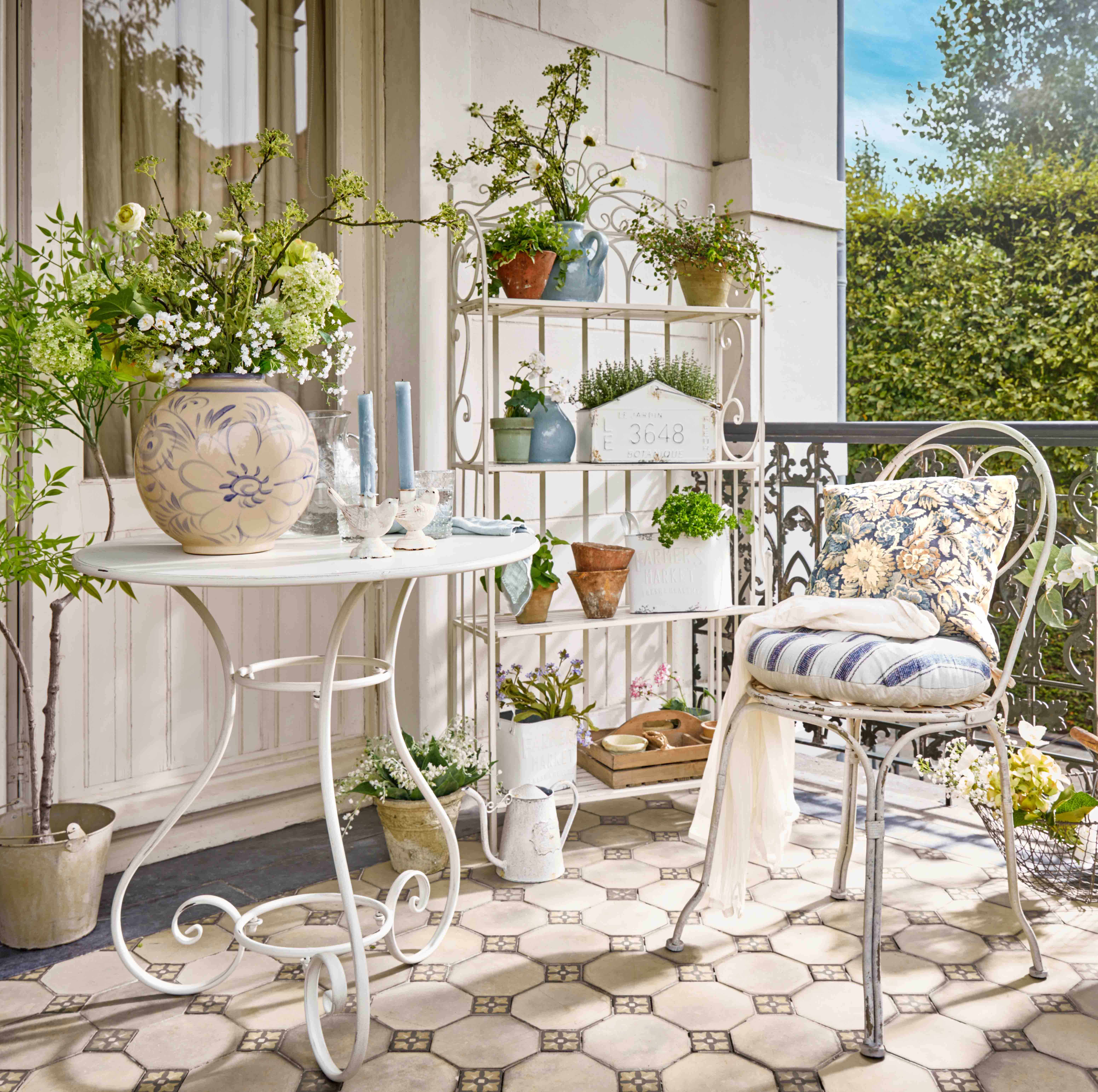 Étagère en métal blanc avec plantes en pots et bougies décoratives sur terrasse fleurie