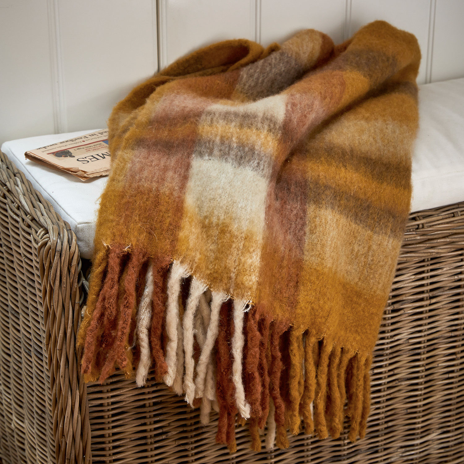 Plaid Alborg Plaid en laine douce aux tons chauds marron et beige avec franges sur fauteuil en osier
