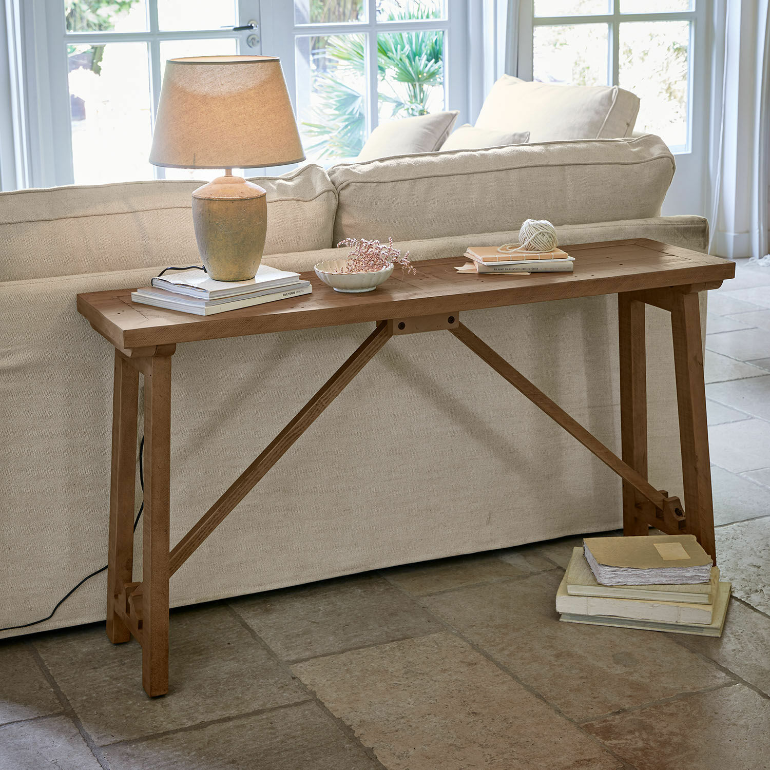 Console Flemming Table en bois naturel derrière un canapé avec lampe et livres, meuble élégant pour salon lumineux