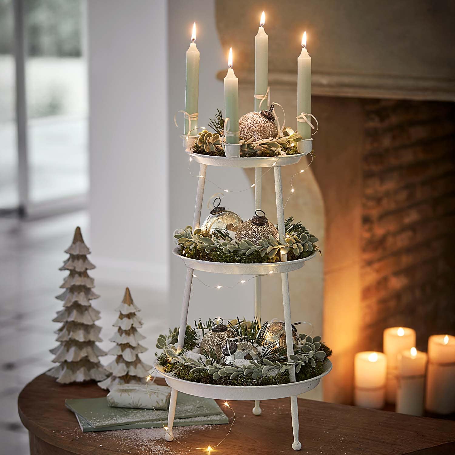 Décoration de Noël blanche à trois niveaux en métal avec branches vertes et bougies allumées sur table
