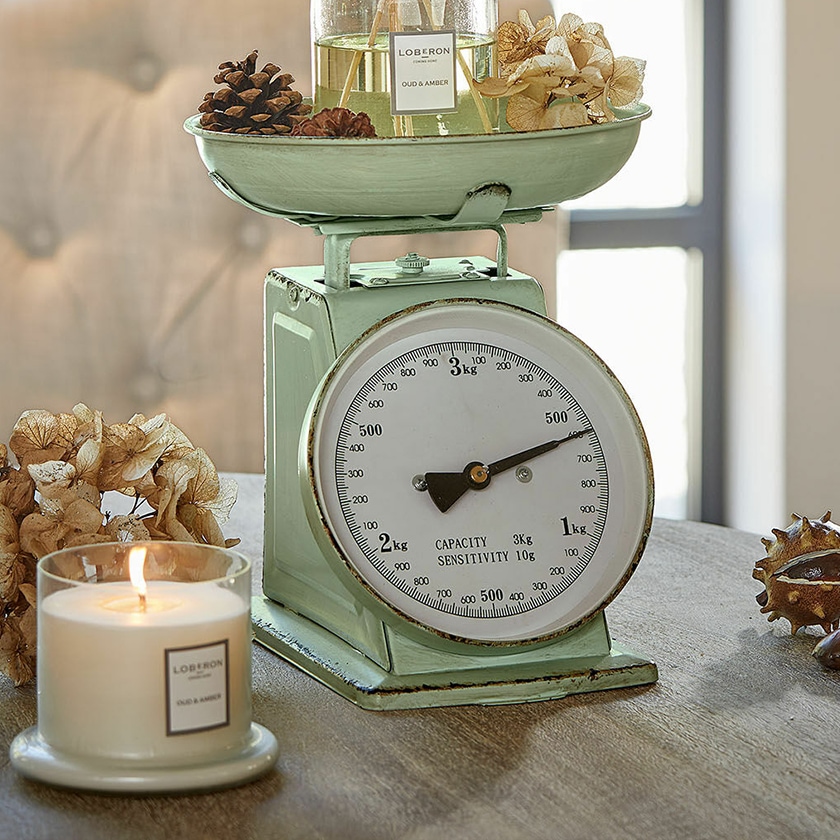 Balance de cuisine en métal vert menthe avec cadran blanc et décorations sur table en bois