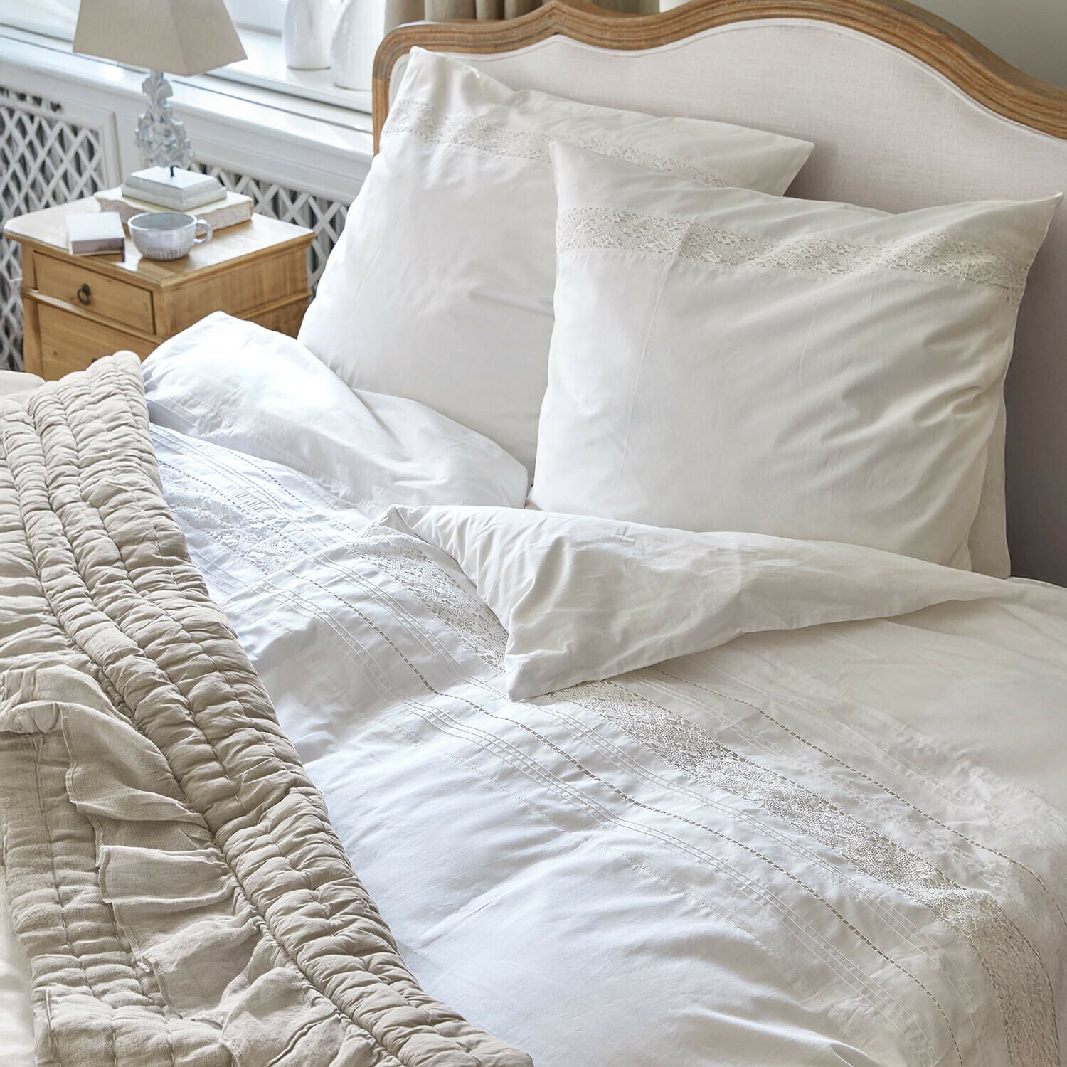 Parure de lit Isolineas Parure de lit blanche avec dentelle sur un lit en bois clair et couverture beige