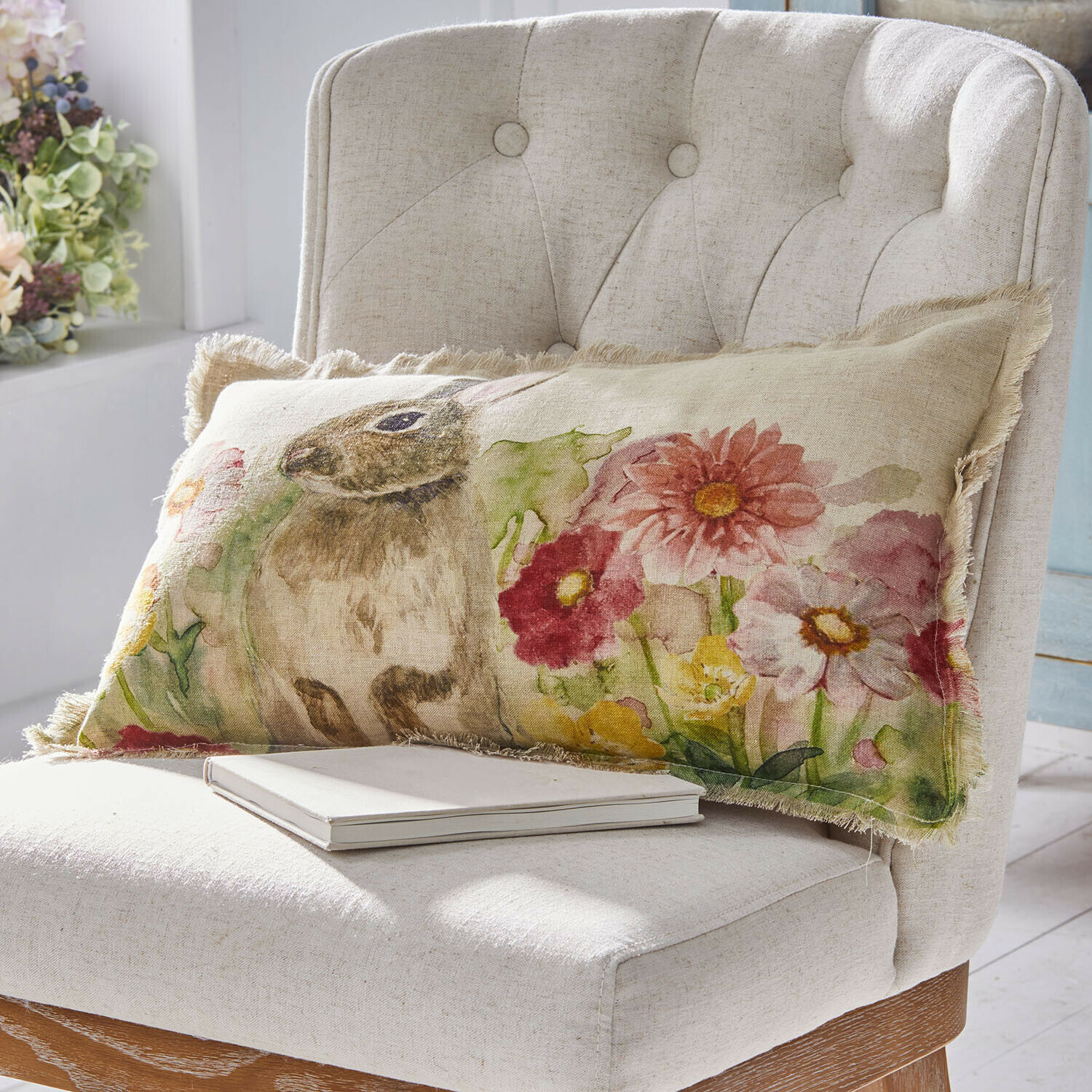 Housse de coussin Parélys Coussin rectangulaire en lin avec motif lapin et fleurs colorées sur fauteuil beige clair