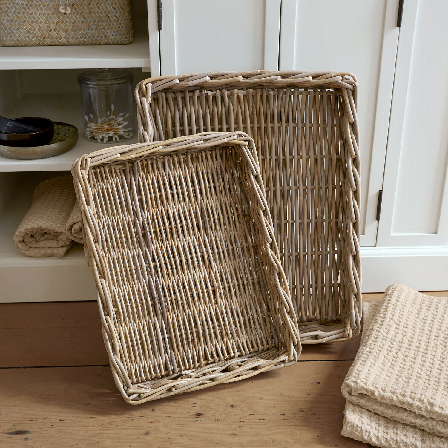 Lot de 2 plateaux Elvendia Deux paniers rectangulaires en rotin naturel posés sur un sol en bois dans un intérieur clair