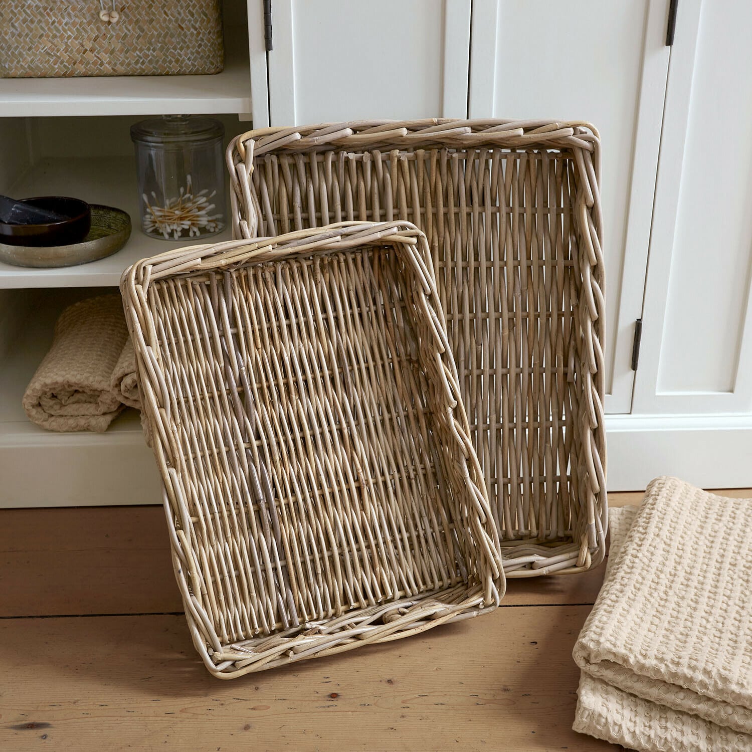 Lot de 2 plateaux Elvendia Deux paniers rectangulaires en rotin naturel posés sur un sol en bois dans un intérieur clair