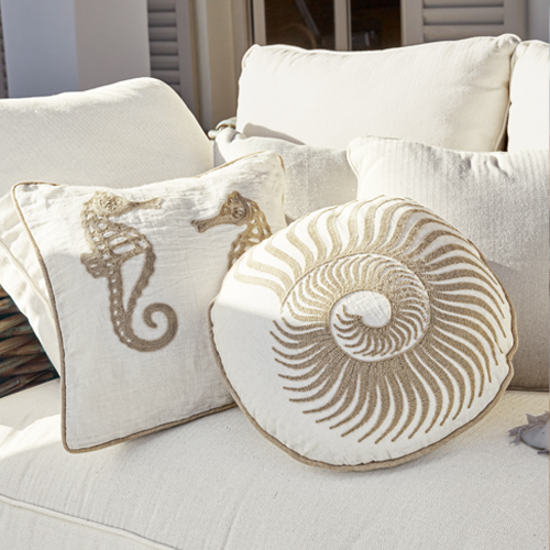 Coussins décoratifs avec motifs marins sur tissu crème posés sur un canapé, style bord de mer