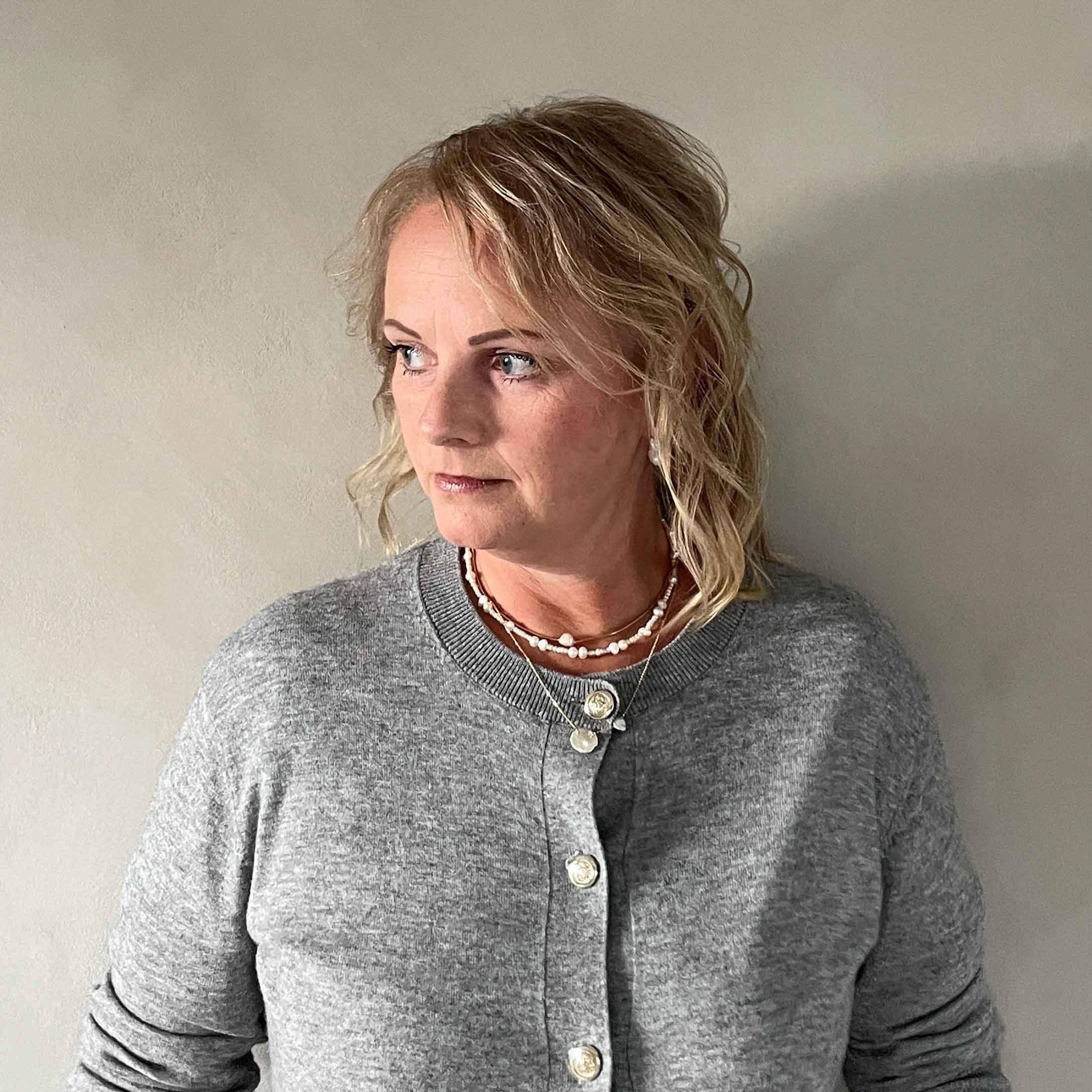 Femme portant un cardigan gris à boutons et des colliers, style décontracté sur fond clair