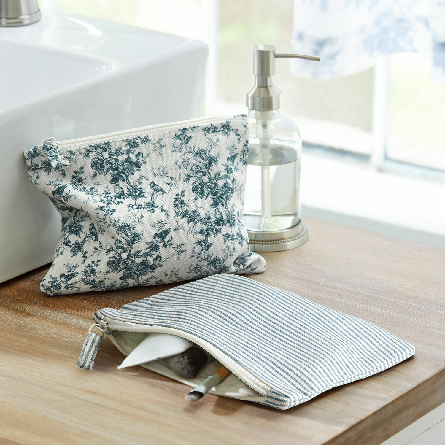 Lot de 2 pochettes Emilie Deux trousses en coton à rayures bleues et motif floral posées sur un plan en bois près du lavabo
