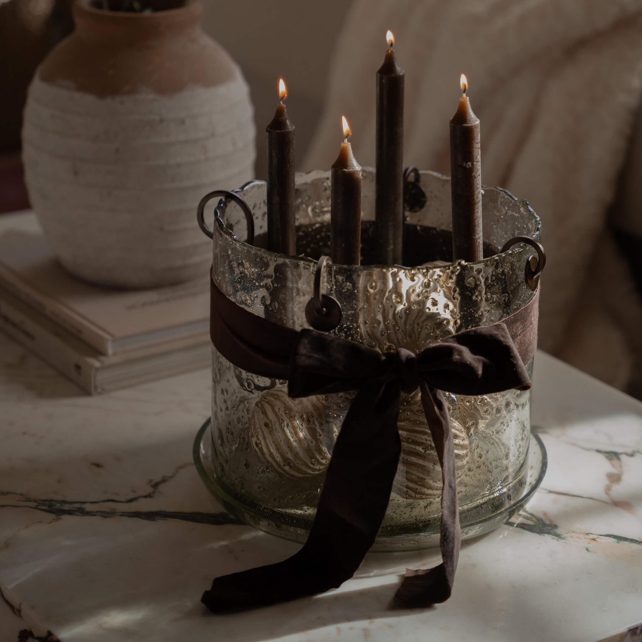 Bougeoir en verre avec quatre bougies noires et un ruban marron sur une table en marbre