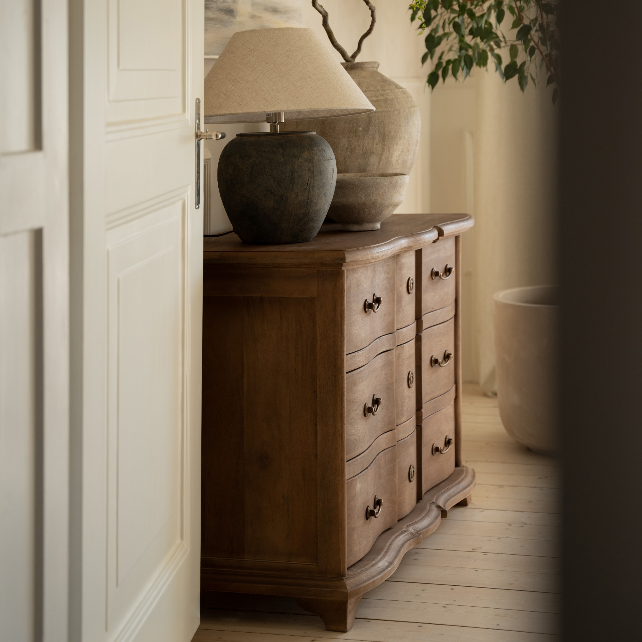 Commode en bois avec tiroirs décoratifs et lampe à abat-jour beige dans un intérieur chaleureux