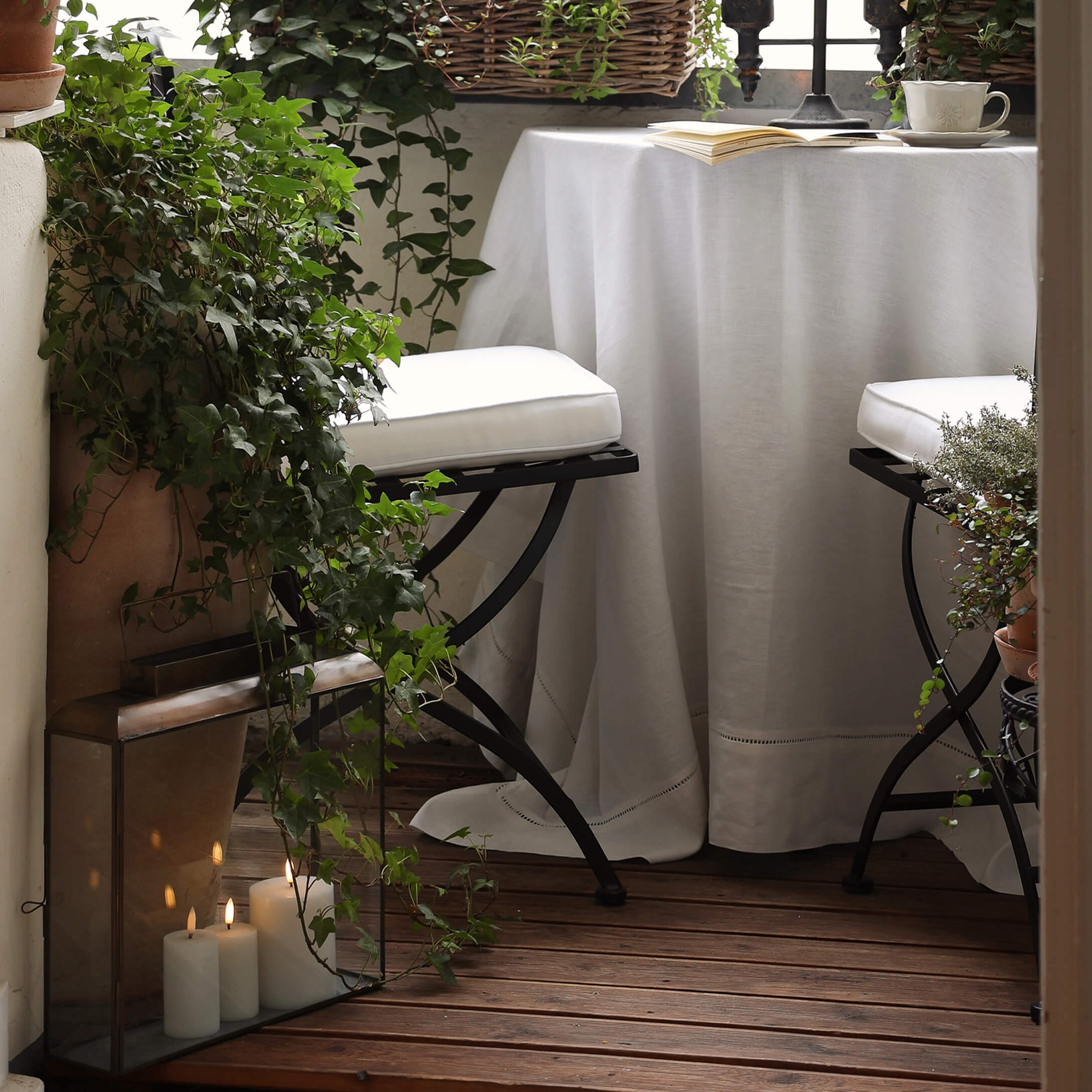Balcon chaleureux avec plancher en bois, nappe blanche et chaises en métal avec coussins blancs