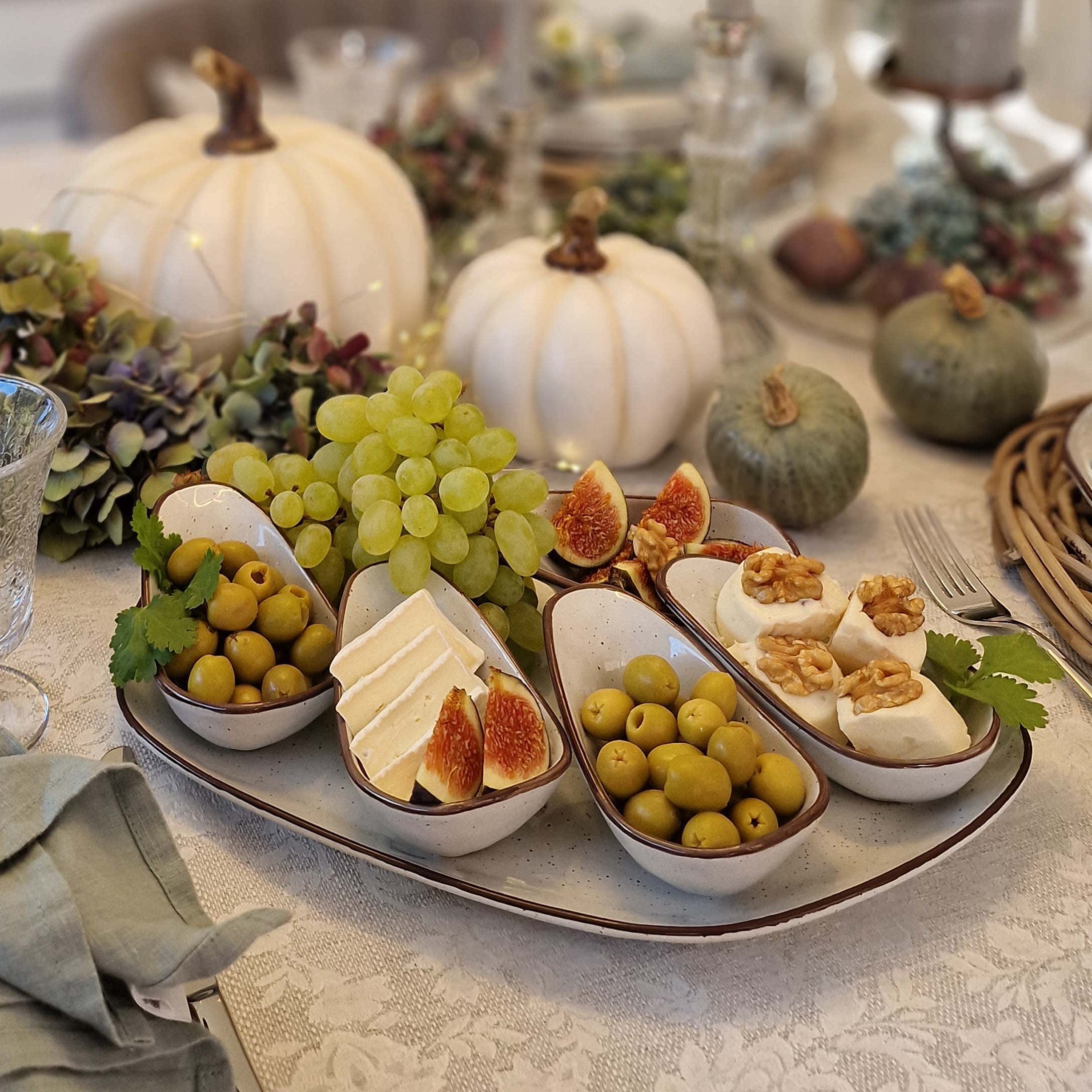 Plateau en céramique blanche avec cinq coupelles contenant olives, fromage et figues sur table décorée