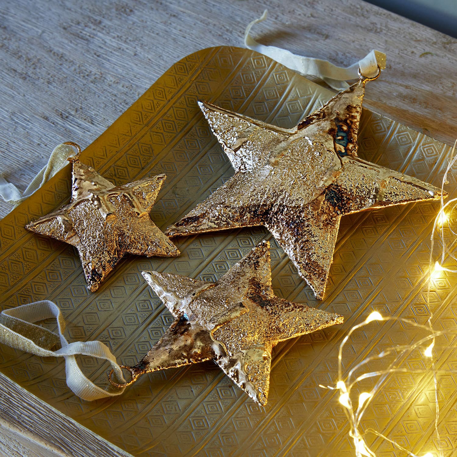 Set de 3 pendentifs Myrska Ensemble de trois étoiles décoratives en métal doré sur un plateau doré avec guirlande lumineuse LED