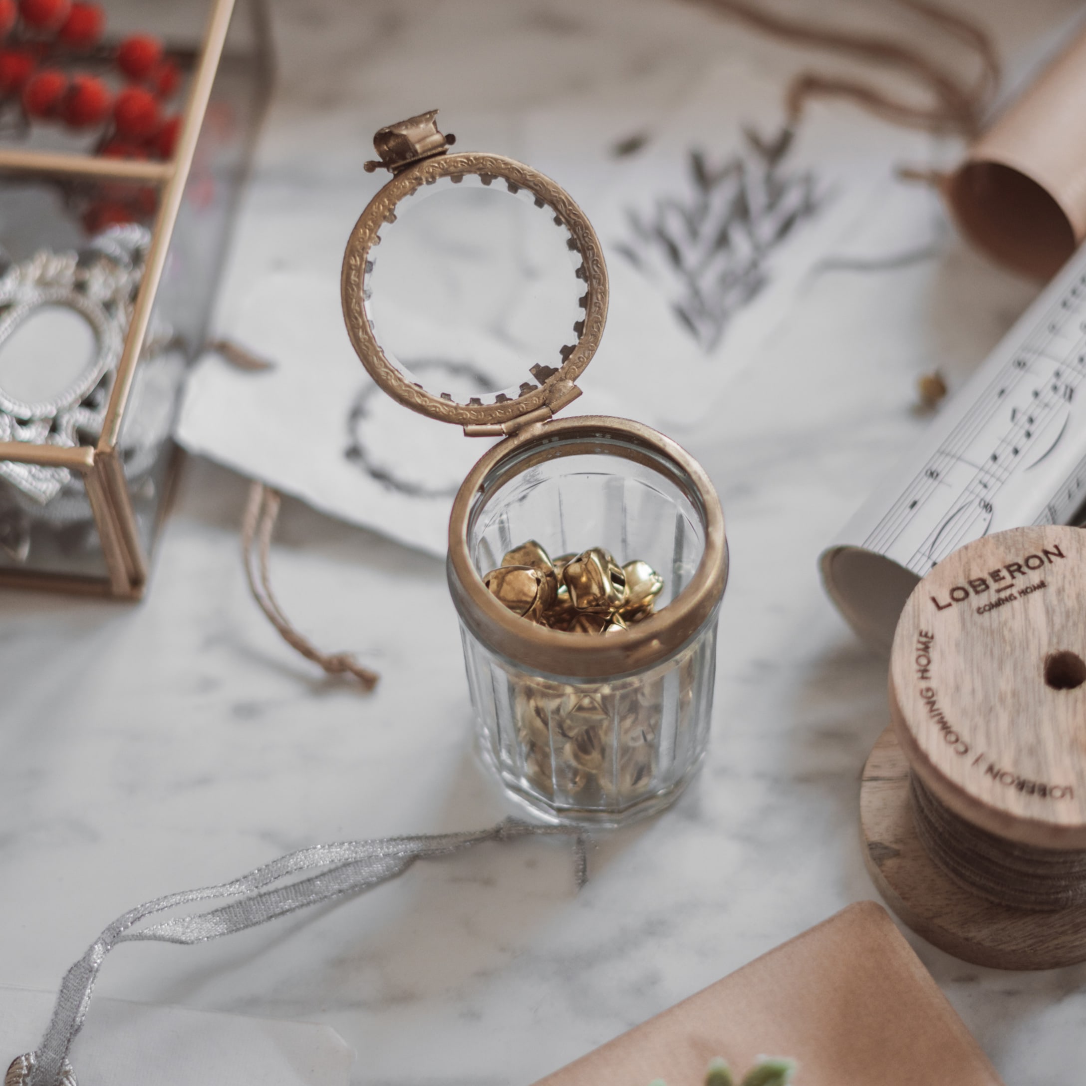 Petit pot en verre avec couvercle en laiton et clochettes dorées sur un plan de travail en marbre, décoration festive