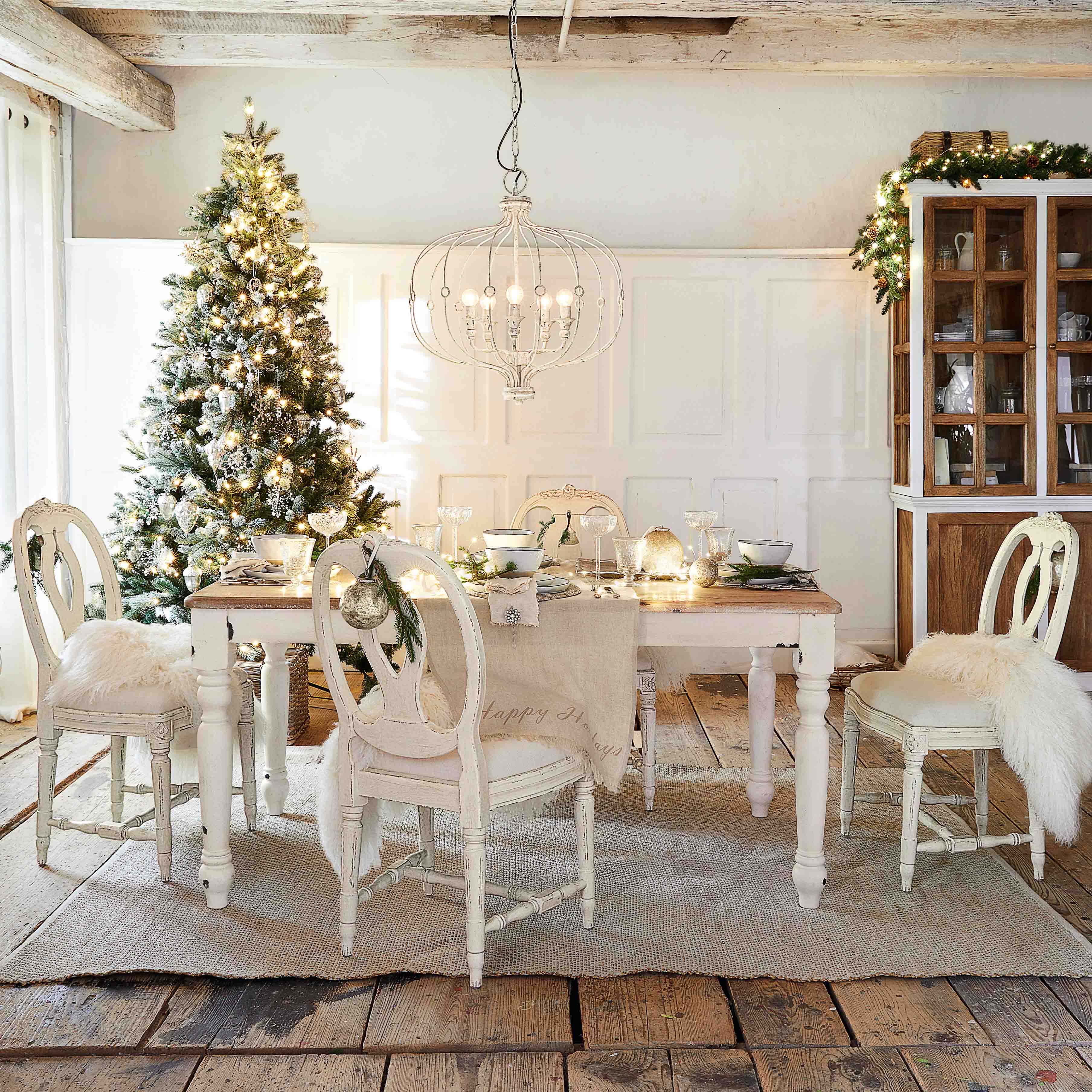 Salle à manger rustique avec table et chaises blanches en bois, décorations de Noël avec sapin et suspension lumineuse