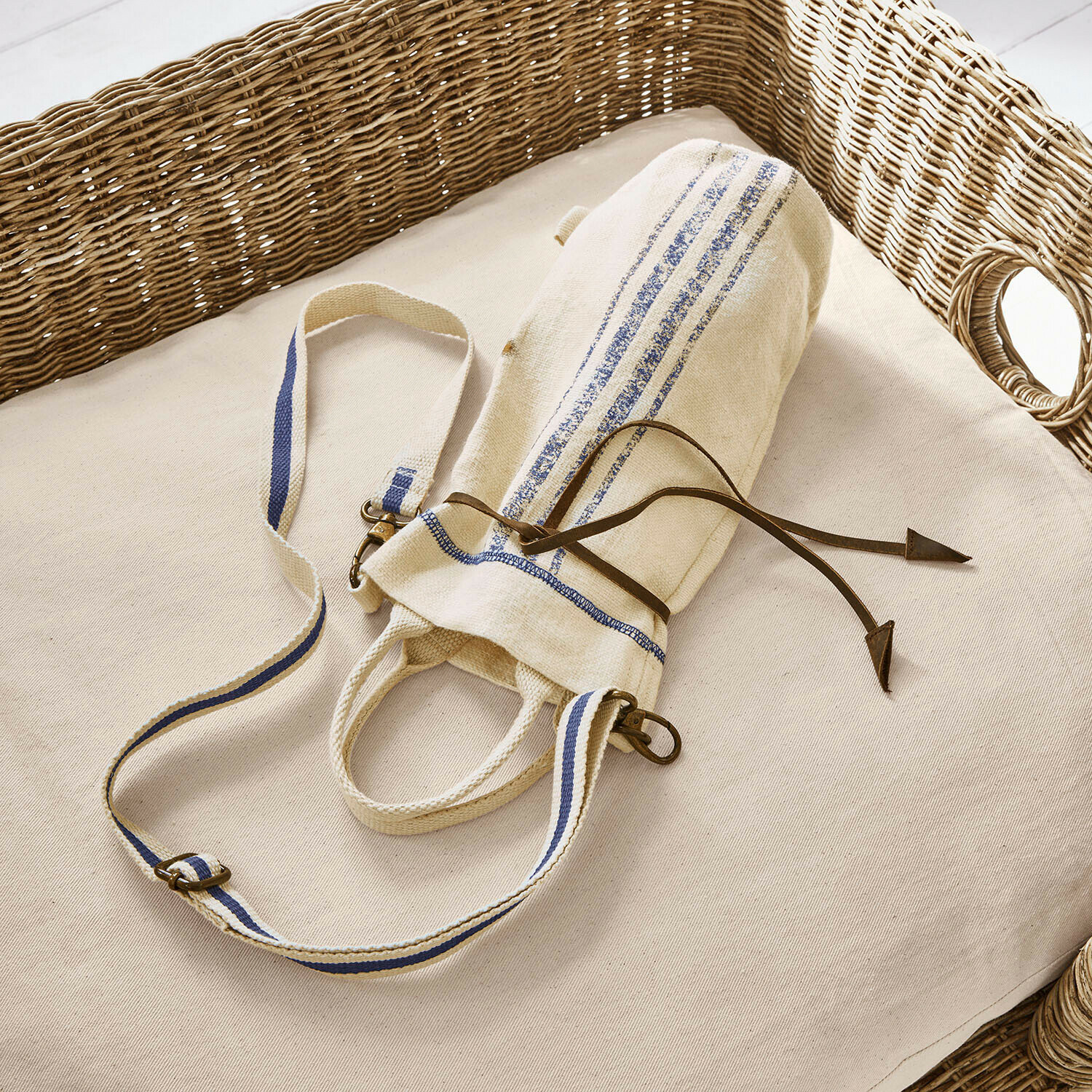 Sac en coton beige avec bandes bleues et cordon en cuir sur coussin clair avec dossier en osier