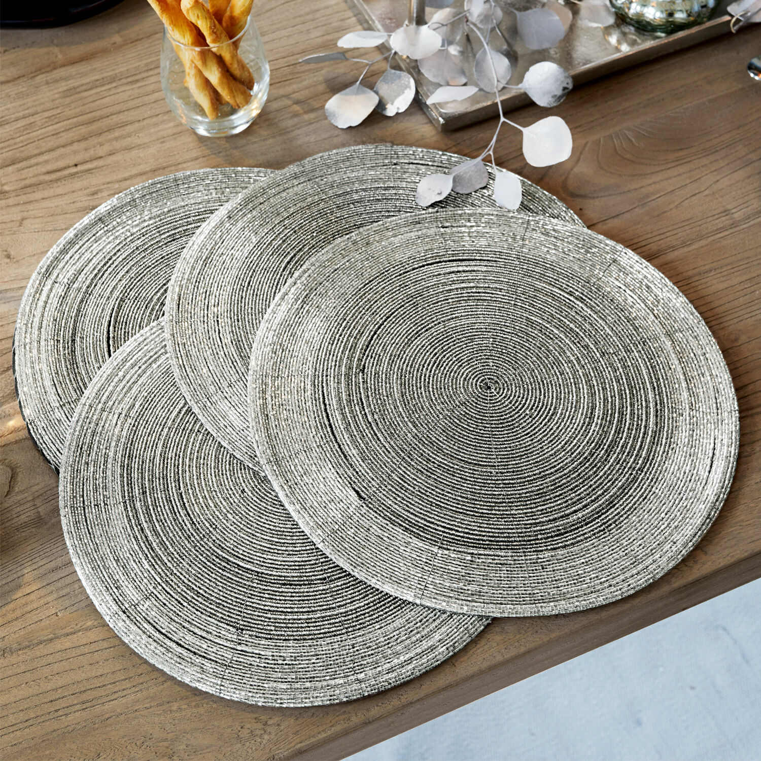 Lot de 4 sets de table Barningham Ensemble de quatre sets de table ronds argentés avec texture tressée sur une table en bois