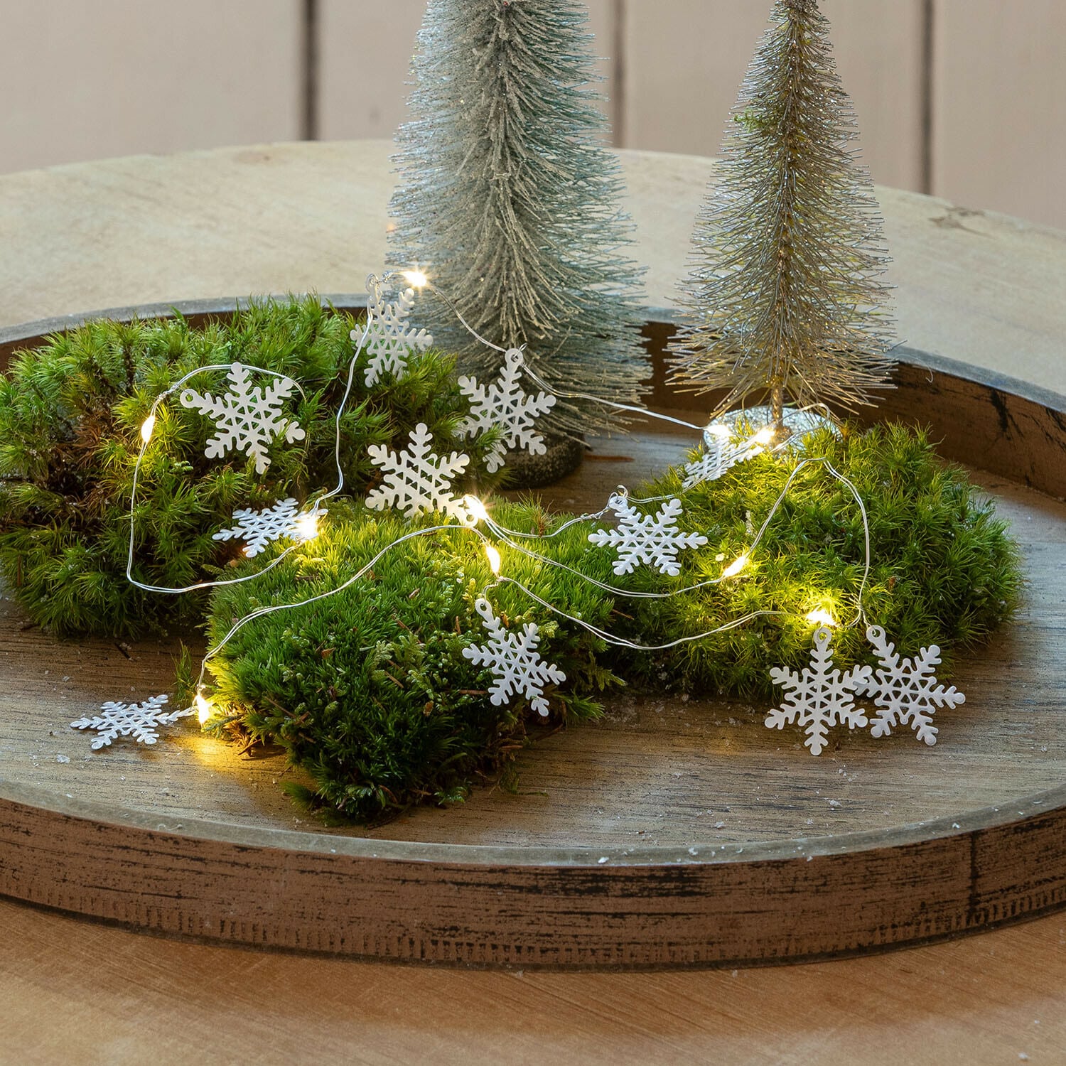 Guirlande lumineuse à LED Azmira Guirlande décorative avec flocons de neige blancs et lumières LED sur mousse verte sur plateau en bois