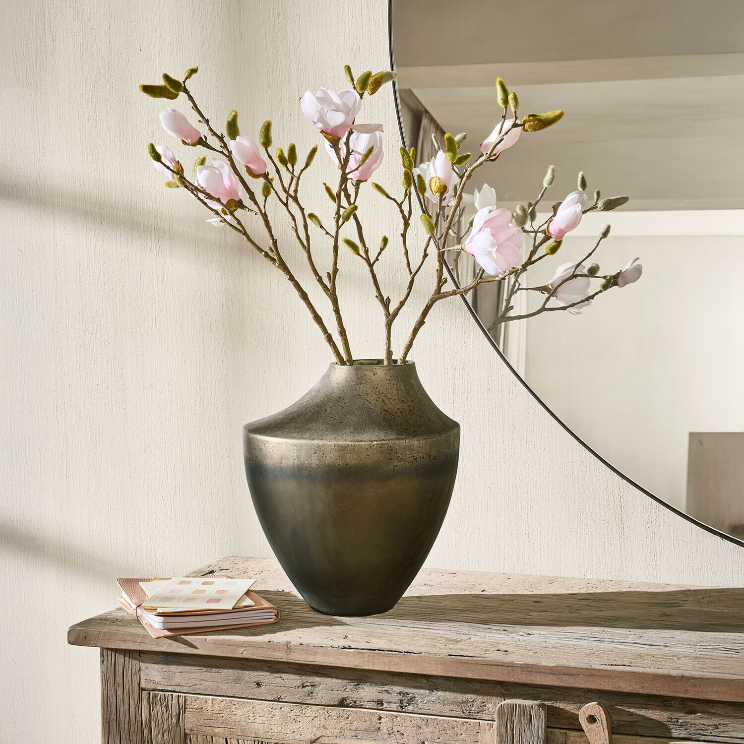 Vase en métal brun foncé avec branches de fleurs roses sur une table en bois rustique