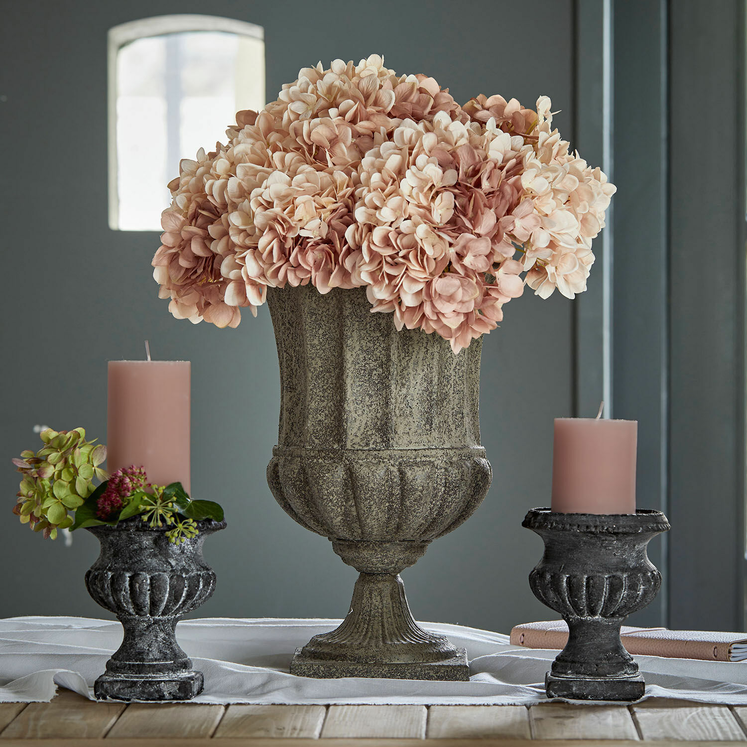 Amphore Renny Vase décoratif en pierre avec fleurs roses et deux bougeoirs noirs avec bougies roses sur table en bois