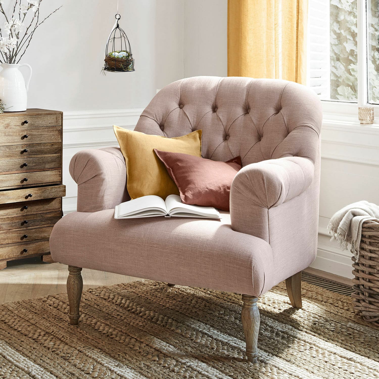 Fauteuil Shambrook Canapé rembourré rose avec pieds en bois et deux coussins colorés sur un tapis tissé naturel
