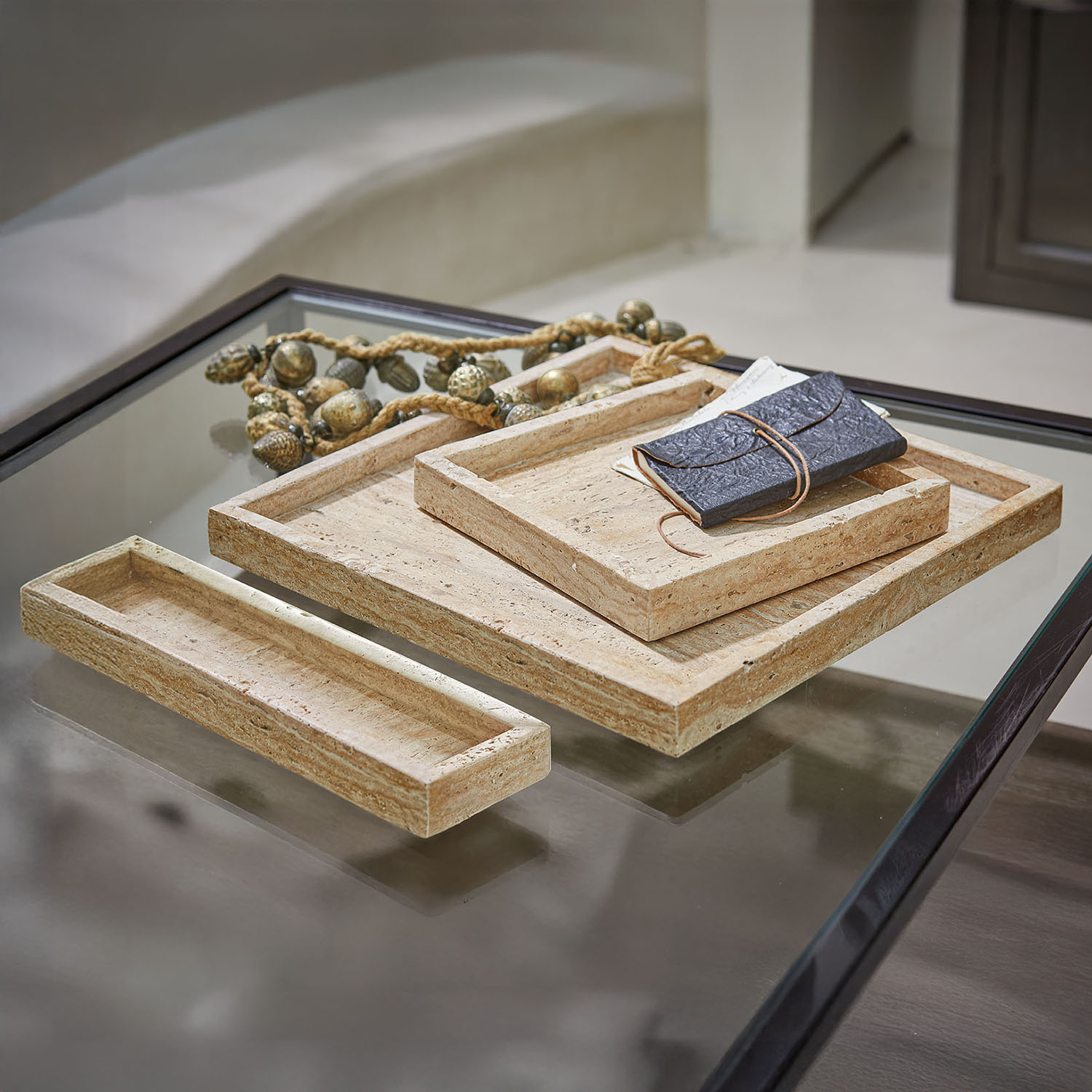 Ensemble de trois plateaux rectangulaires en pierre beige posés sur une table en verre à cadre noir
