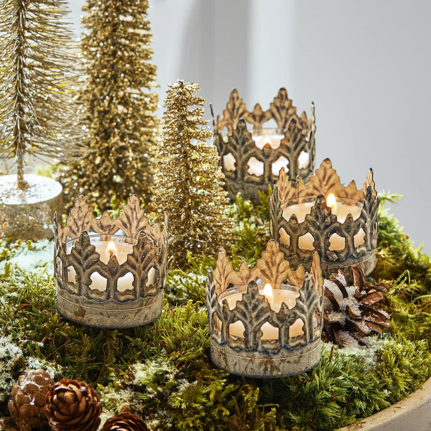 Photophores en métal en forme de couronne sur mousse verte avec décorations de Noël et sapins dorés