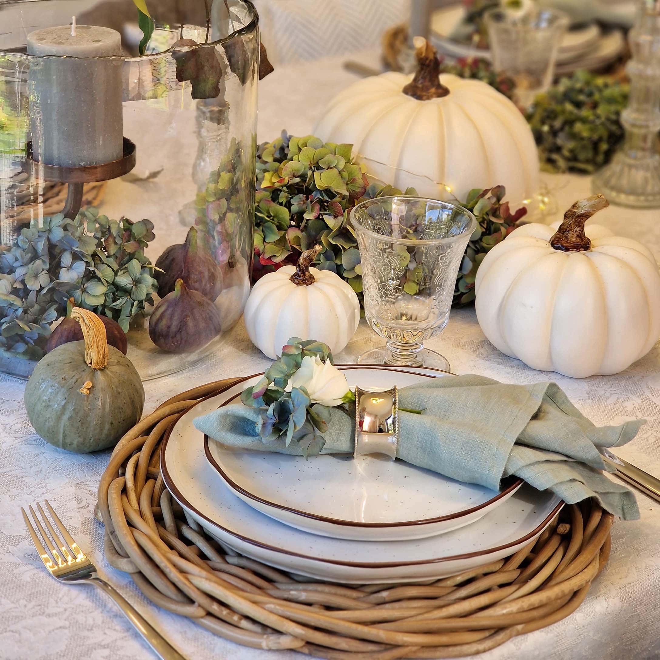 Décoration de table avec citrouilles blanches et vertes, verre et serviette en lin sur assiettes en céramique