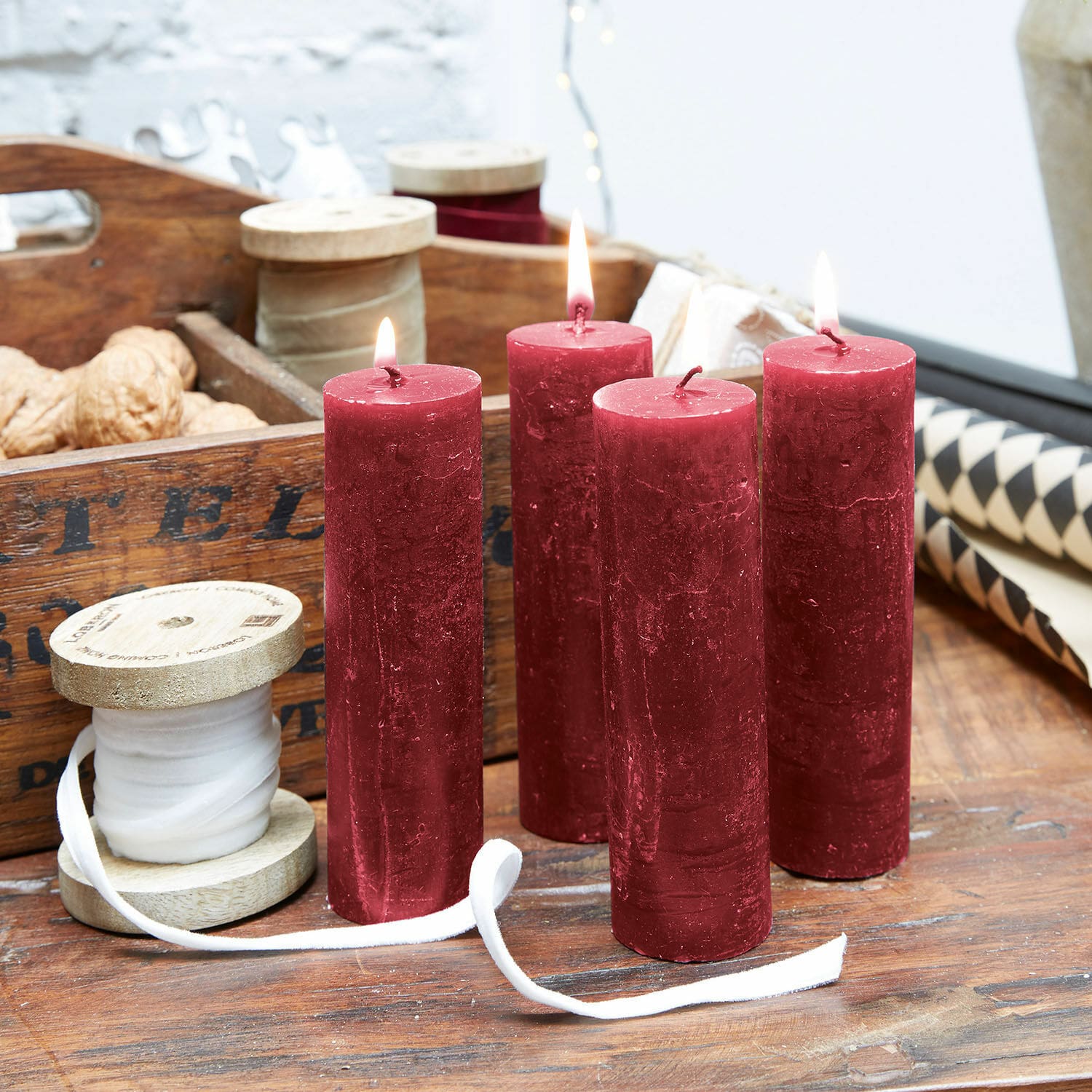 Lot de 4 bougies Muriel Quatre bougies rouges en cire sur une table en bois avec bobines décoratives et noix