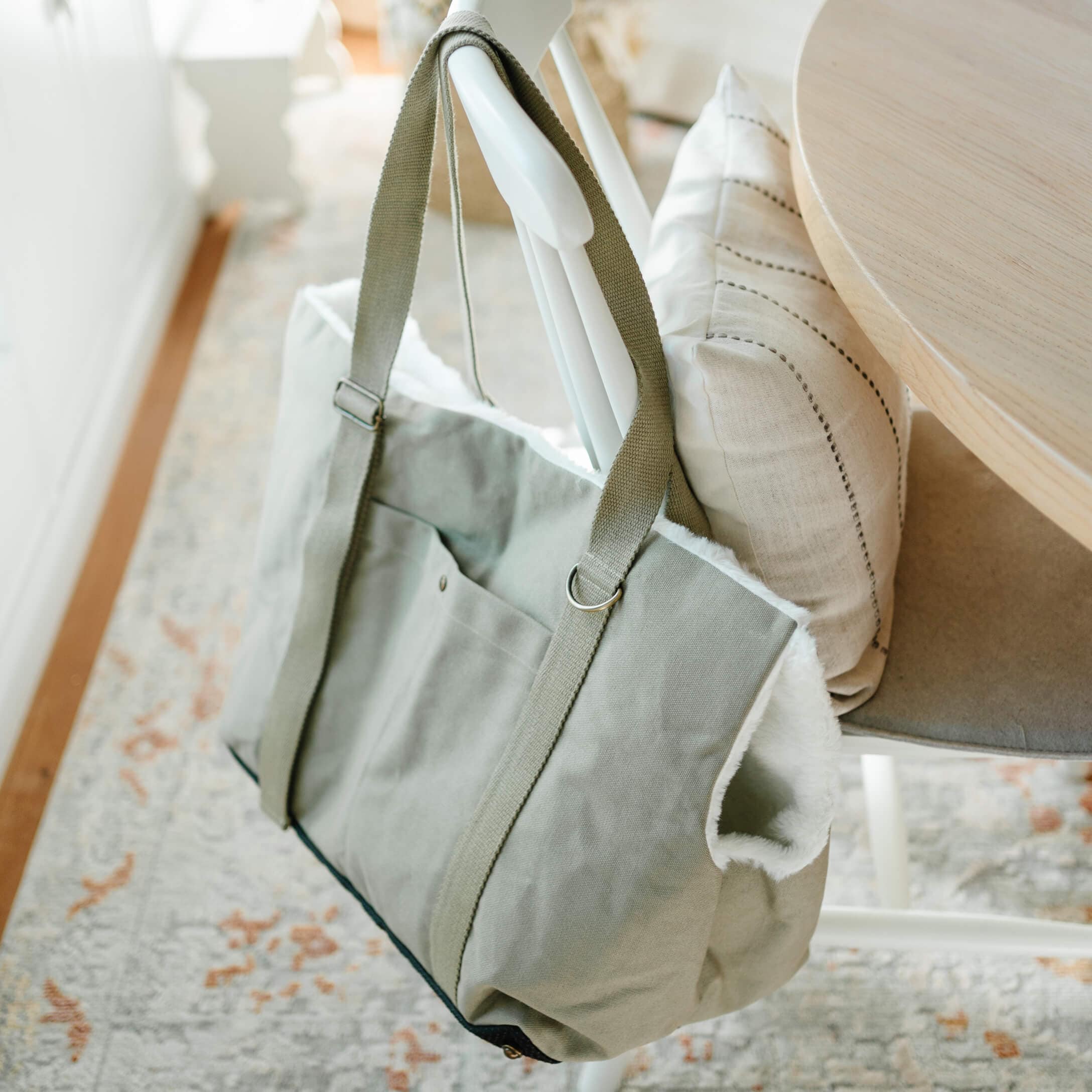 Sac gris en tissu avec intérieur en fausse fourrure blanche suspendu à une chaise blanche dans une pièce lumineuse