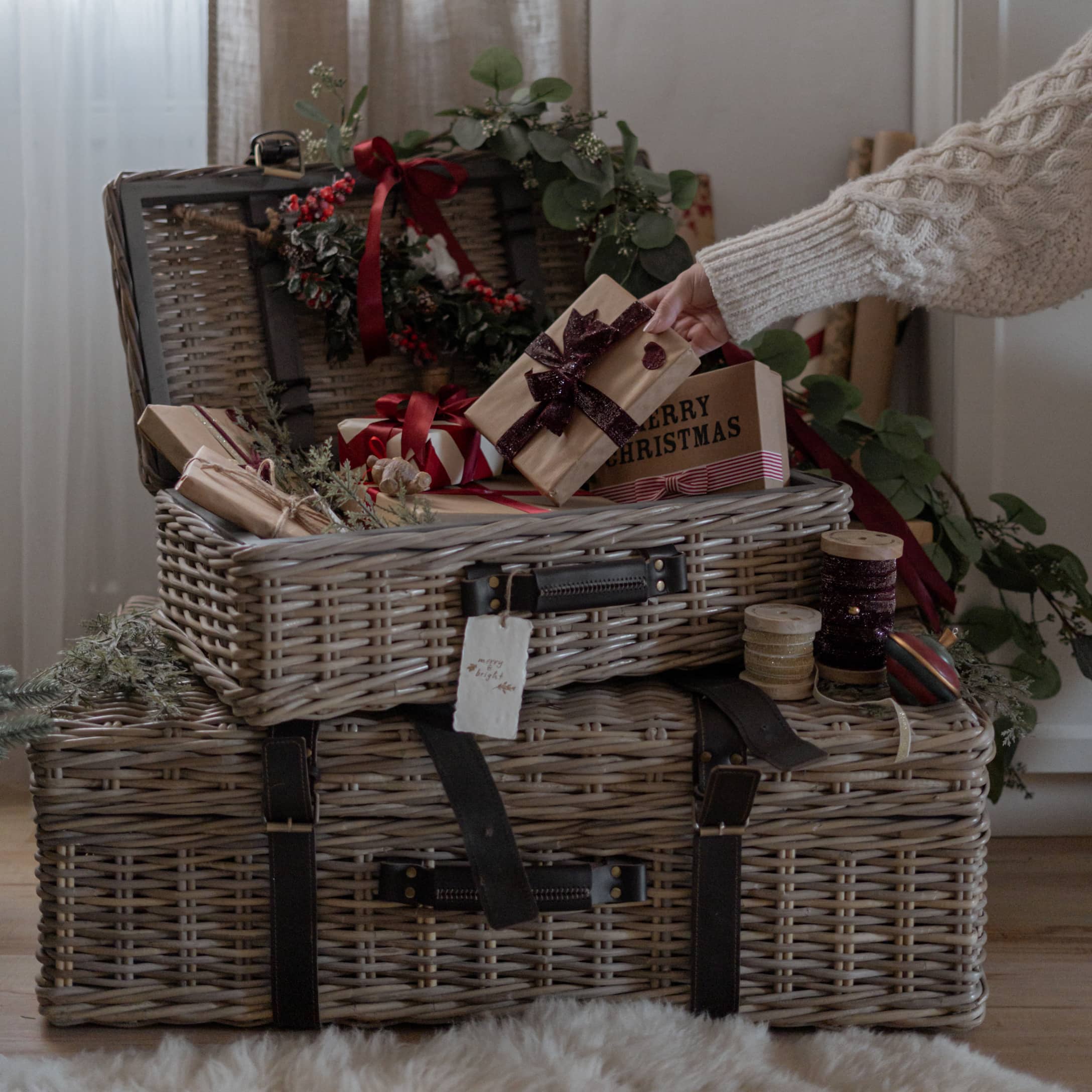 Valises en osier grises avec sangles noires, cadeaux de Noël et décorations festives en arrière-plan